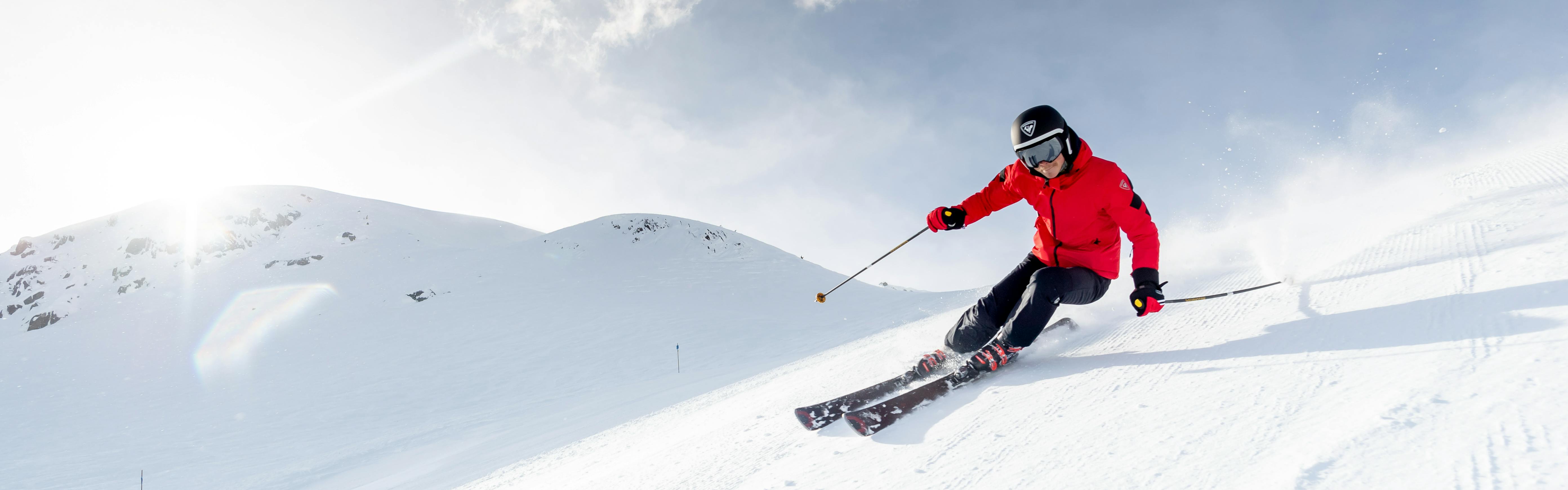 A skier in a red jacket and Rossignol skis heads downhill.