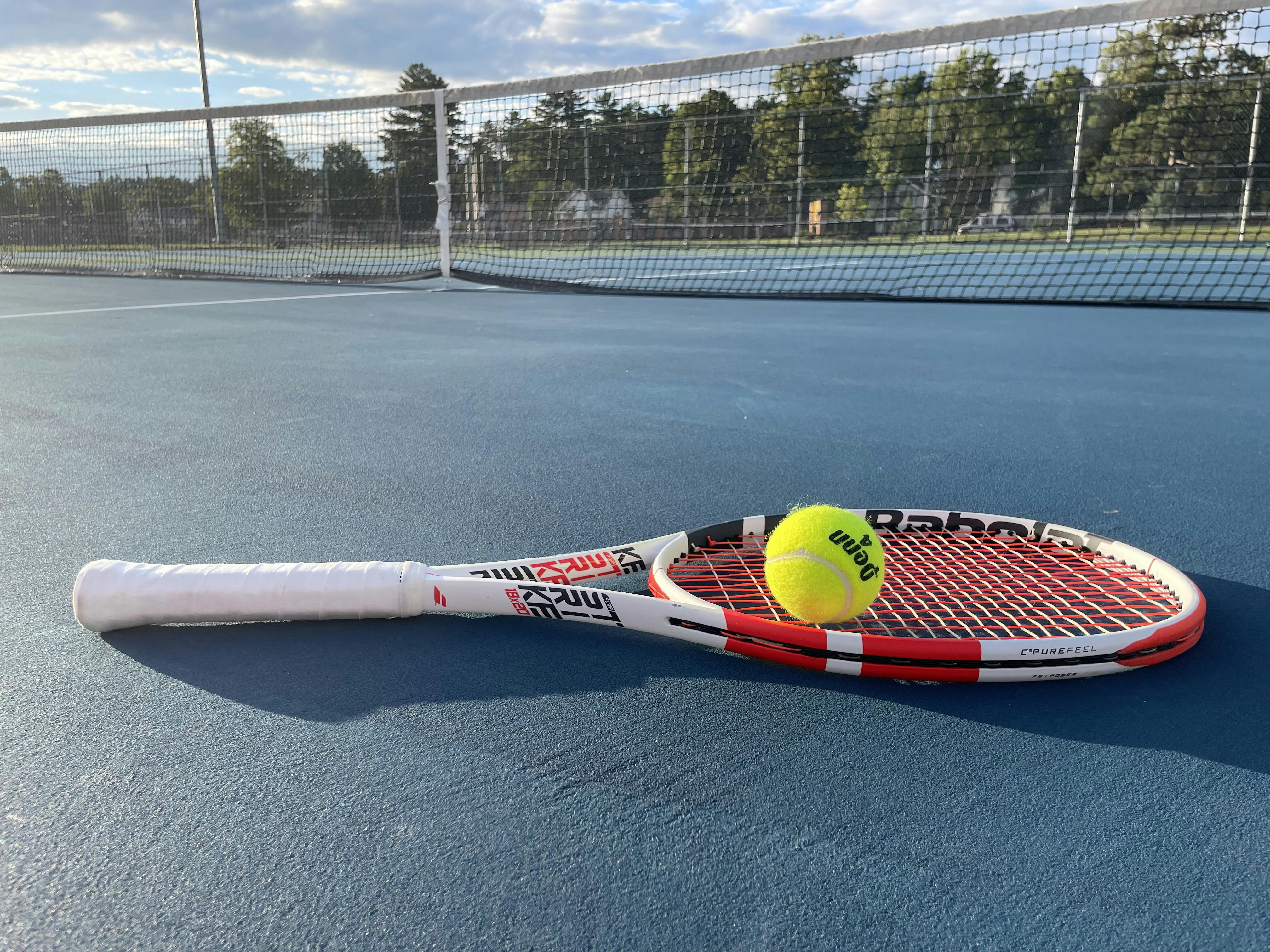 The Babolat Pure Strike 18x20 Racquet lying on the tennis court with a tennis ball.