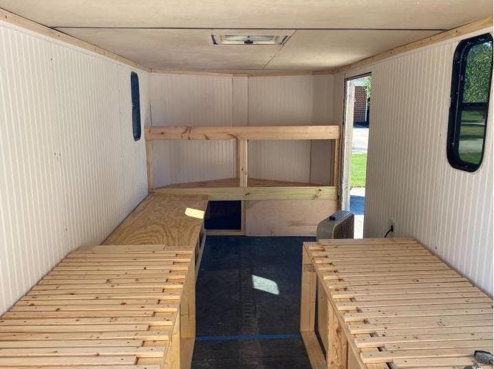 The inside of a finished cargo trailer. There are a few beds and the walls are white. There are two windows.
