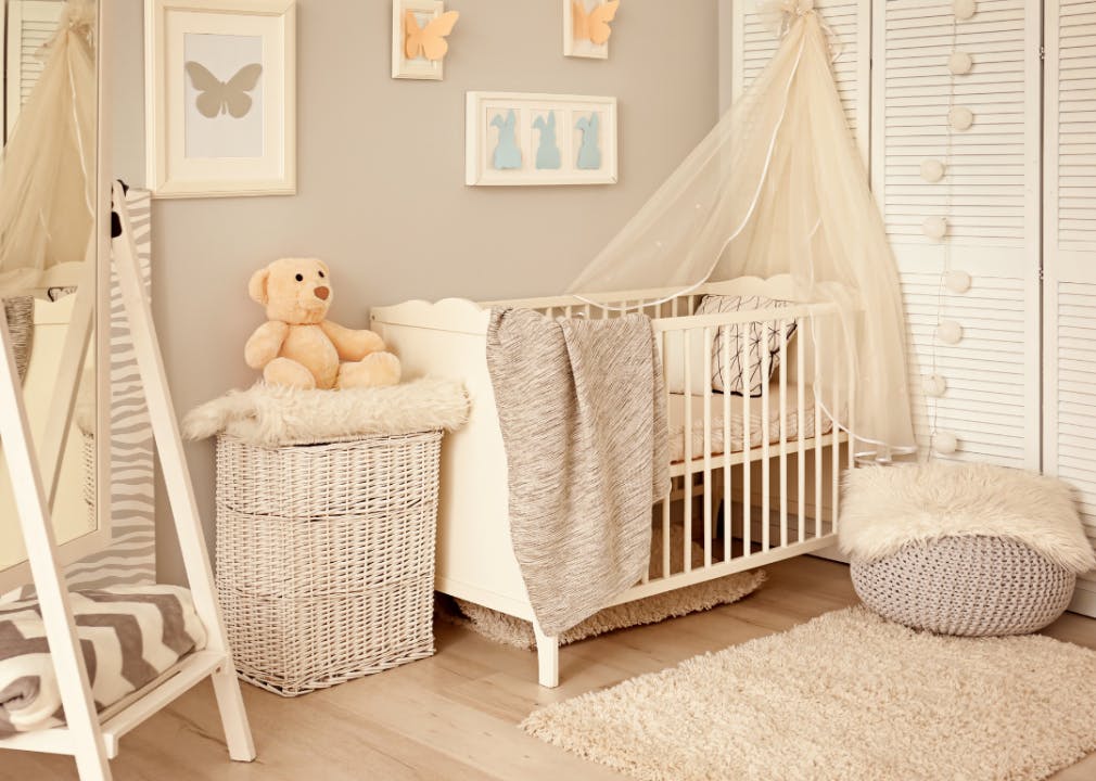 A beige-colored nursery with a crib, chair, wall hangings, and stuffed teddy bear