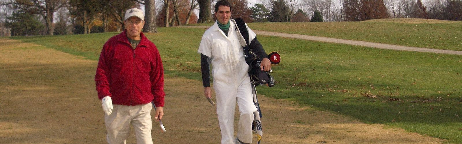 A golfer walks holding a club as his caddie carries his bag behind him.