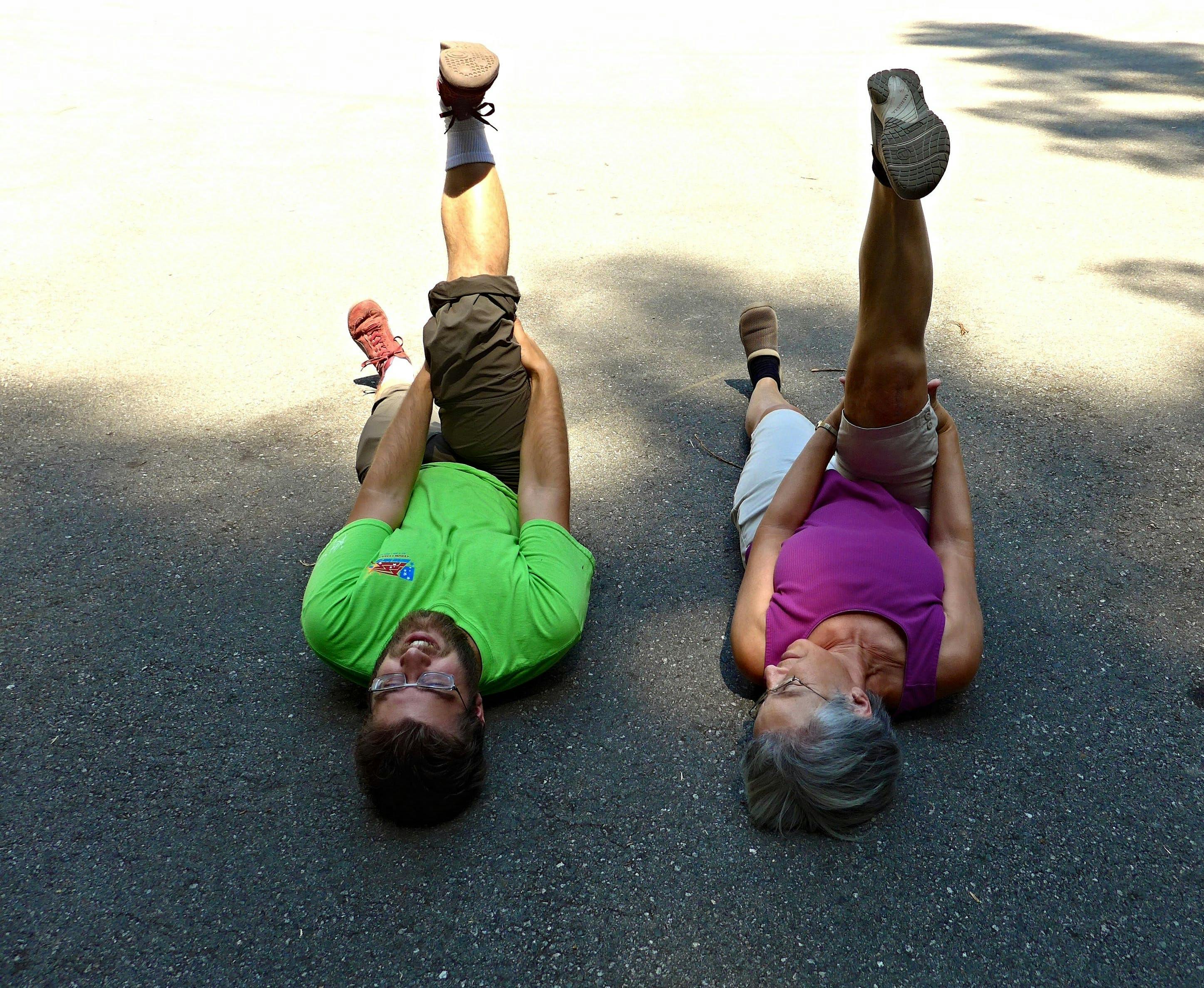 Two hikers lay on their backs on the ground as they put one leg in the air to stretch it. 