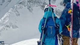 Two skiers with their skis on their backpacks hiking along a ridgeline. 