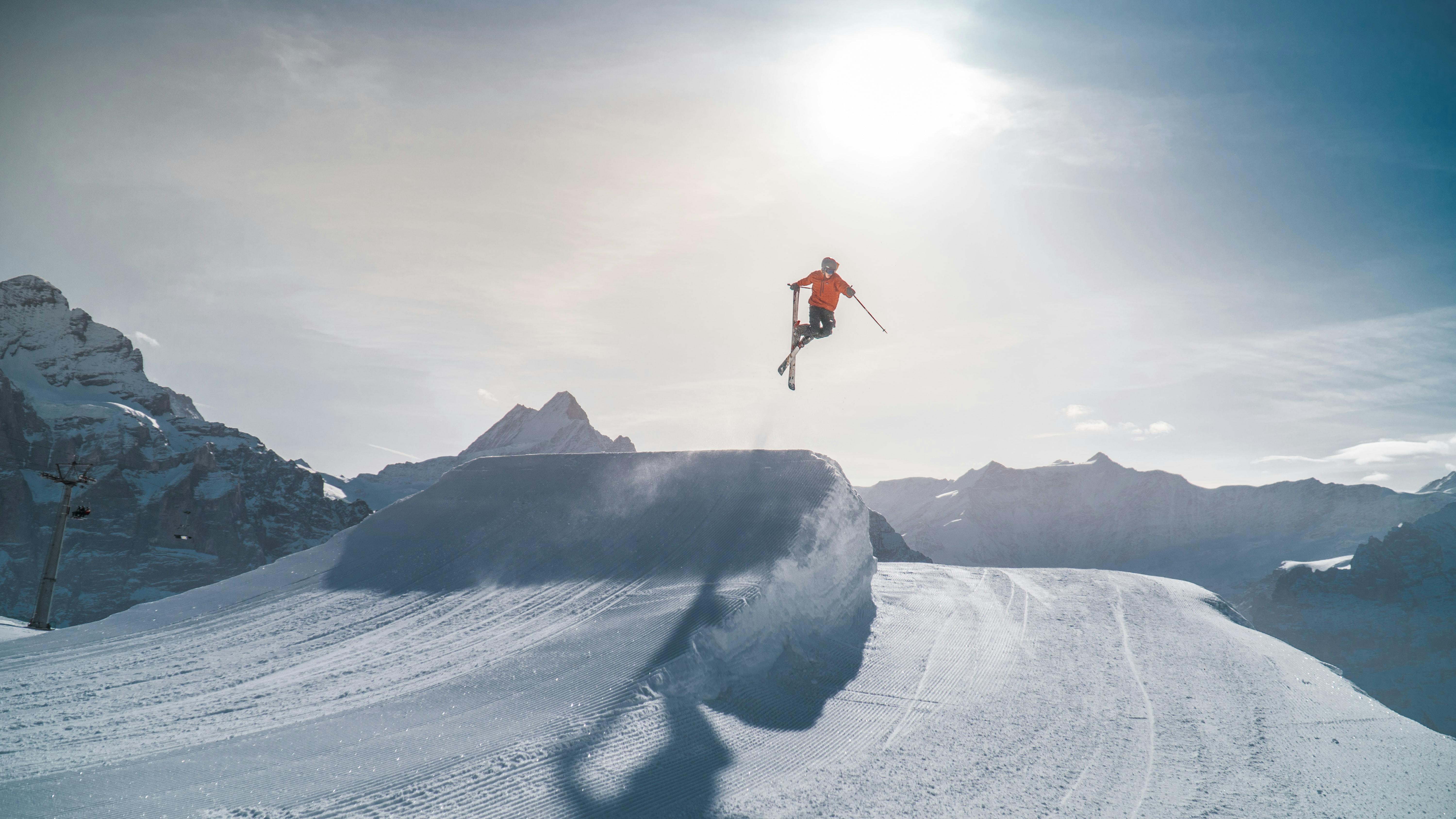 Someone jumps off a ramp with their skis crossing in the air. The skier is small against a vast landscape. 