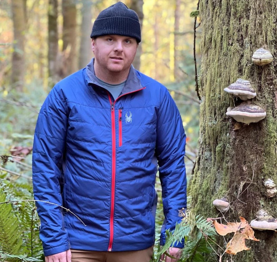 A man standing next to a tree with mushrooms on it while wearing the Spyder Glissade Jacket.