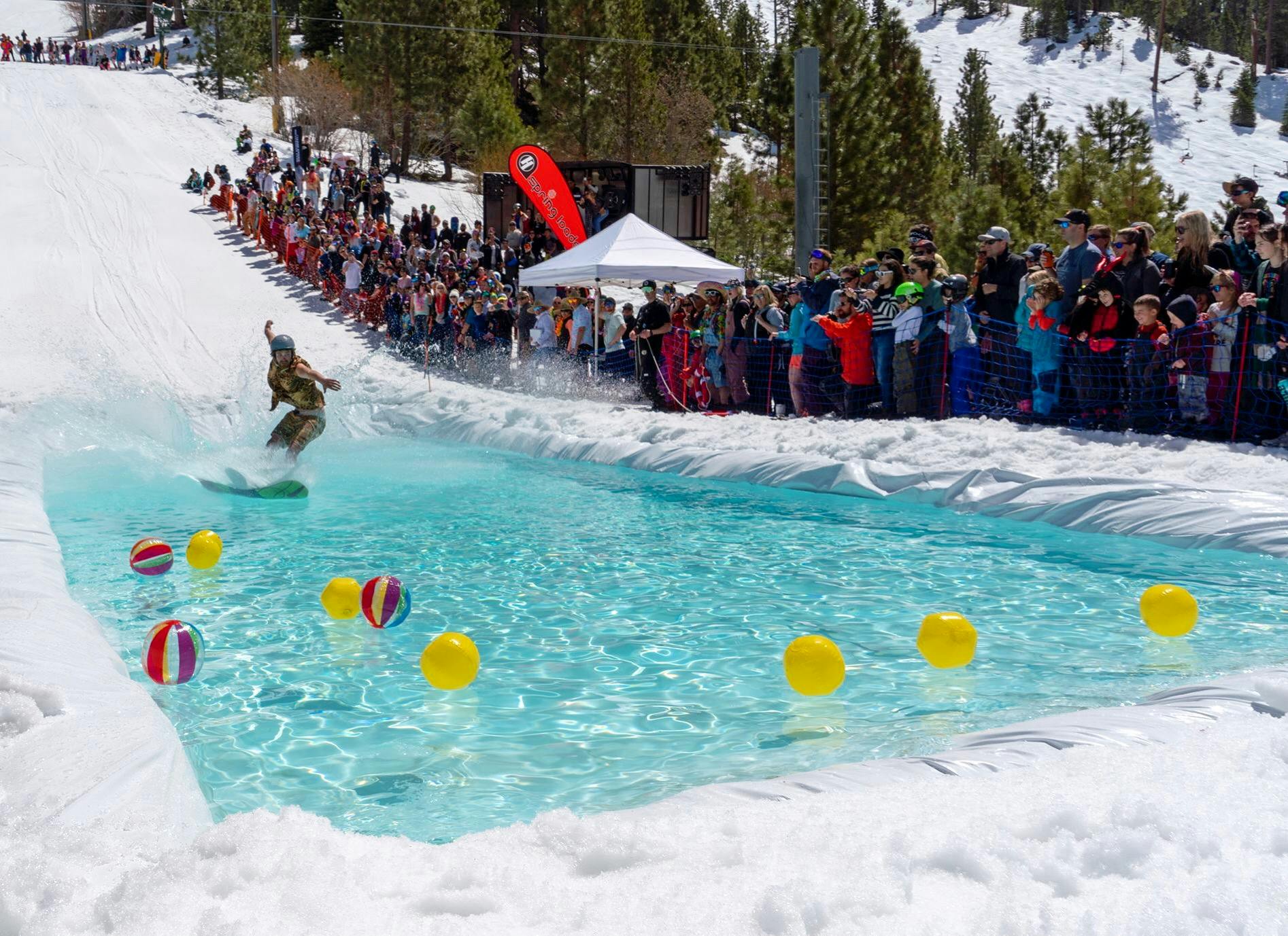 A snowboarder doing a pond skim at a ski resort. 