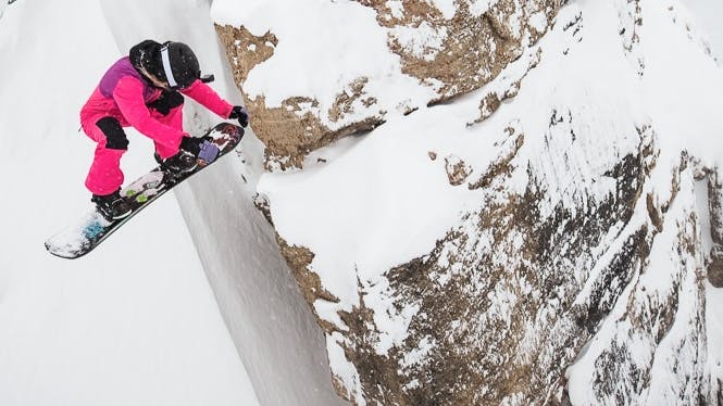 A snowboarder in pink sits at the lip of the coulier. 