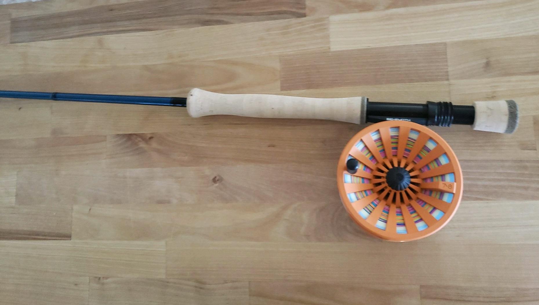 An image of a flyfishing rod with an orange reel against a light, wooden background.