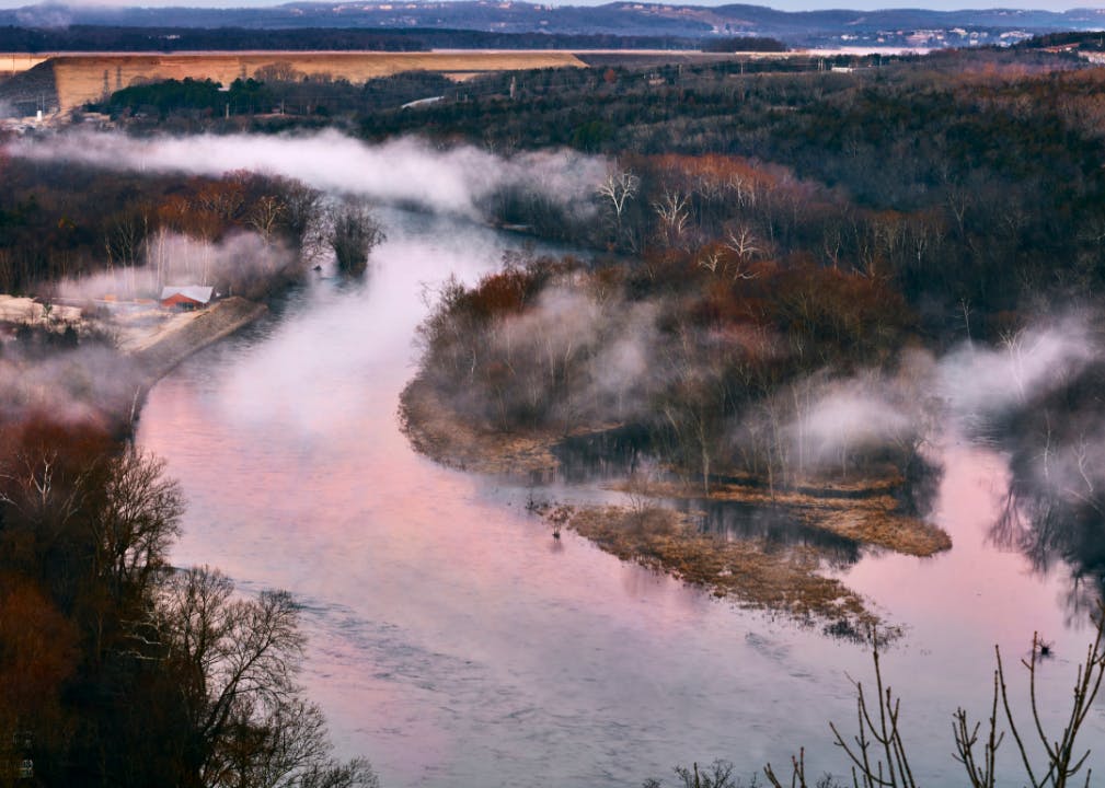Aerial view of a pink sunrise reflected in a winding river topped with wisps of clouds