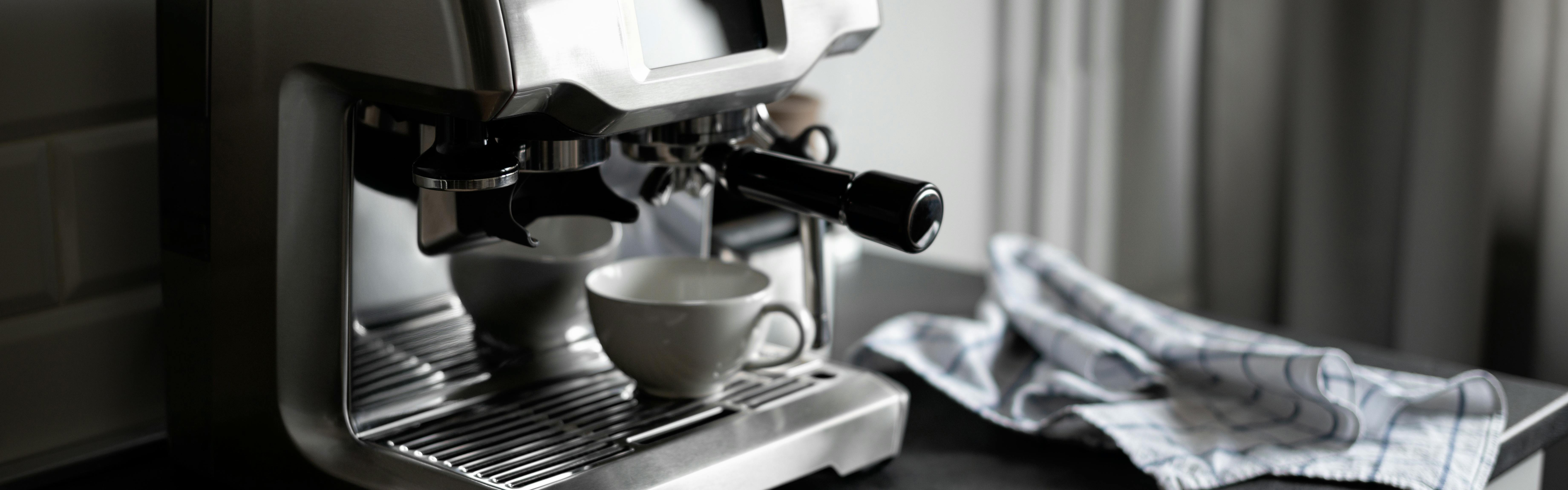 A white espresso cup sits on a stainless steel espresso machine, waiting for the shot. 