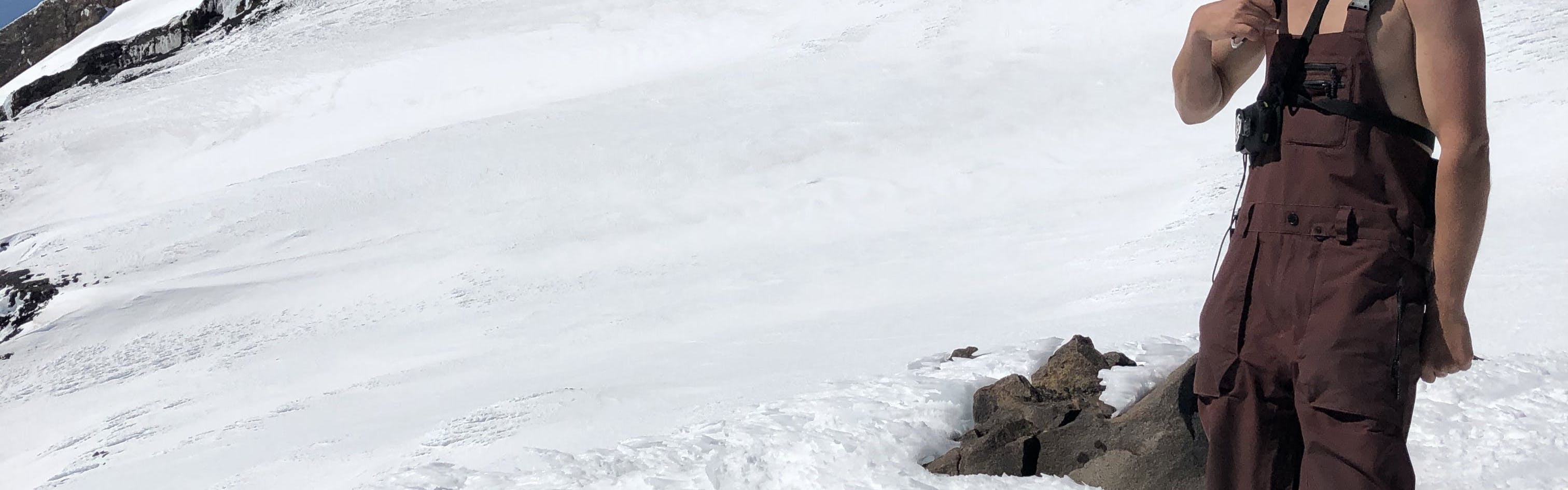 A snowboarder standing on the snow wearing the Volcom Men's Rain GORE-TEX® Bib Pants.