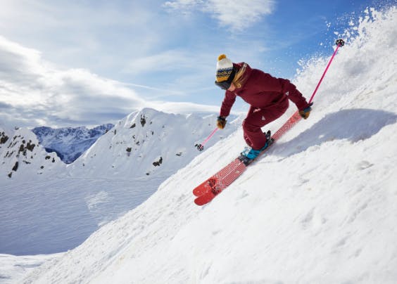 Skier wearing red jacket and pants skis down steep slope with their Black Crow skis. 