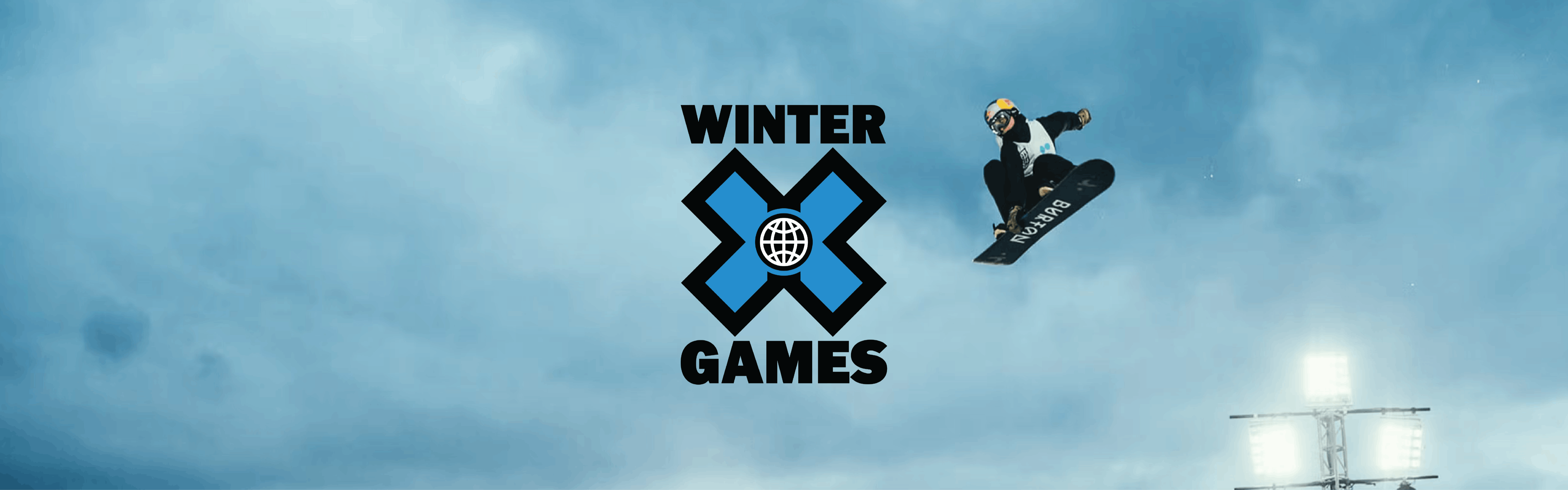 A snowboarder jumps and grabs the bottom of their board in dimming light. Huge stadium lights are illuminated below them. The Winter X Games logo is in the center of the image.