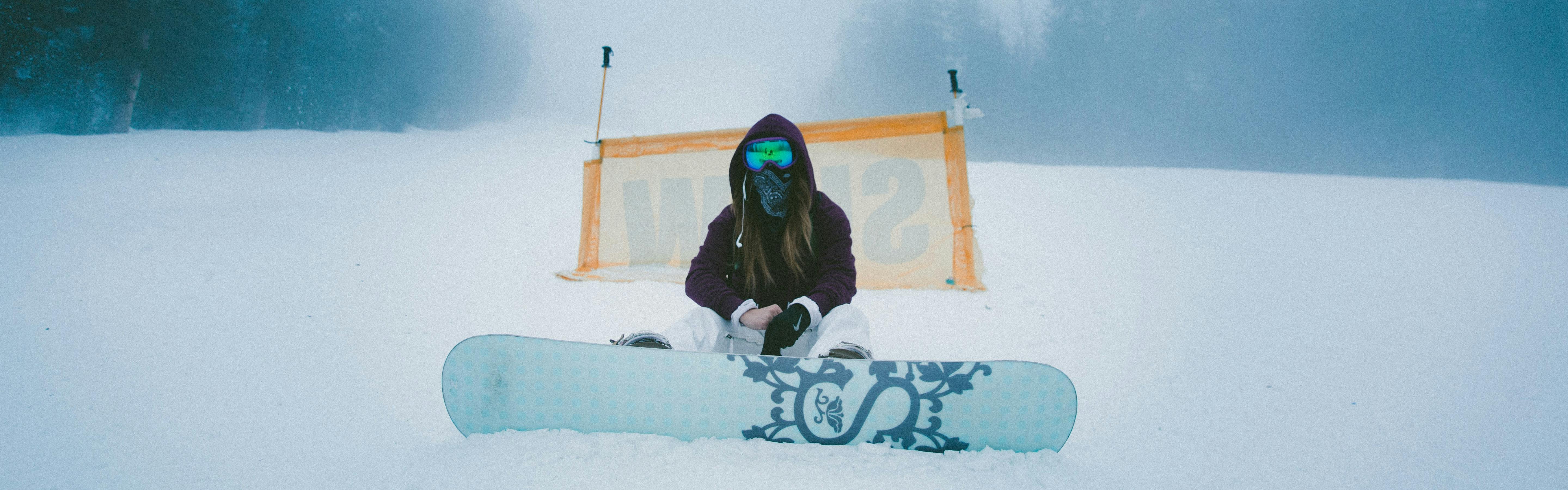 A snowboarder sits in the snow in front of a SLOW sign