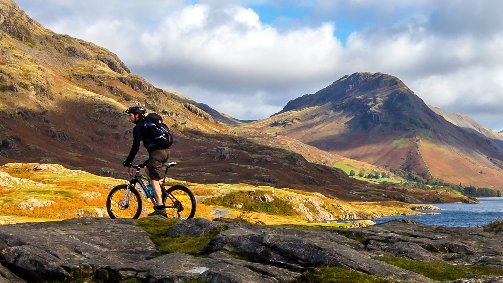 A man on a mountain bike rests among rolling hills and mountains