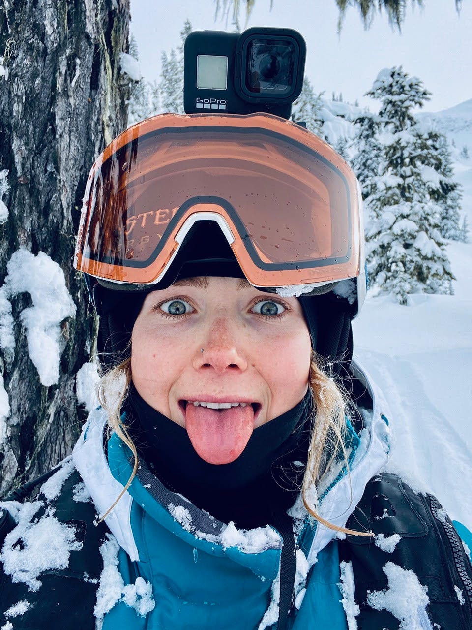 Maggie sticks her tongue out for a snow-covered selfie. She has a GoPro on her helmet. 