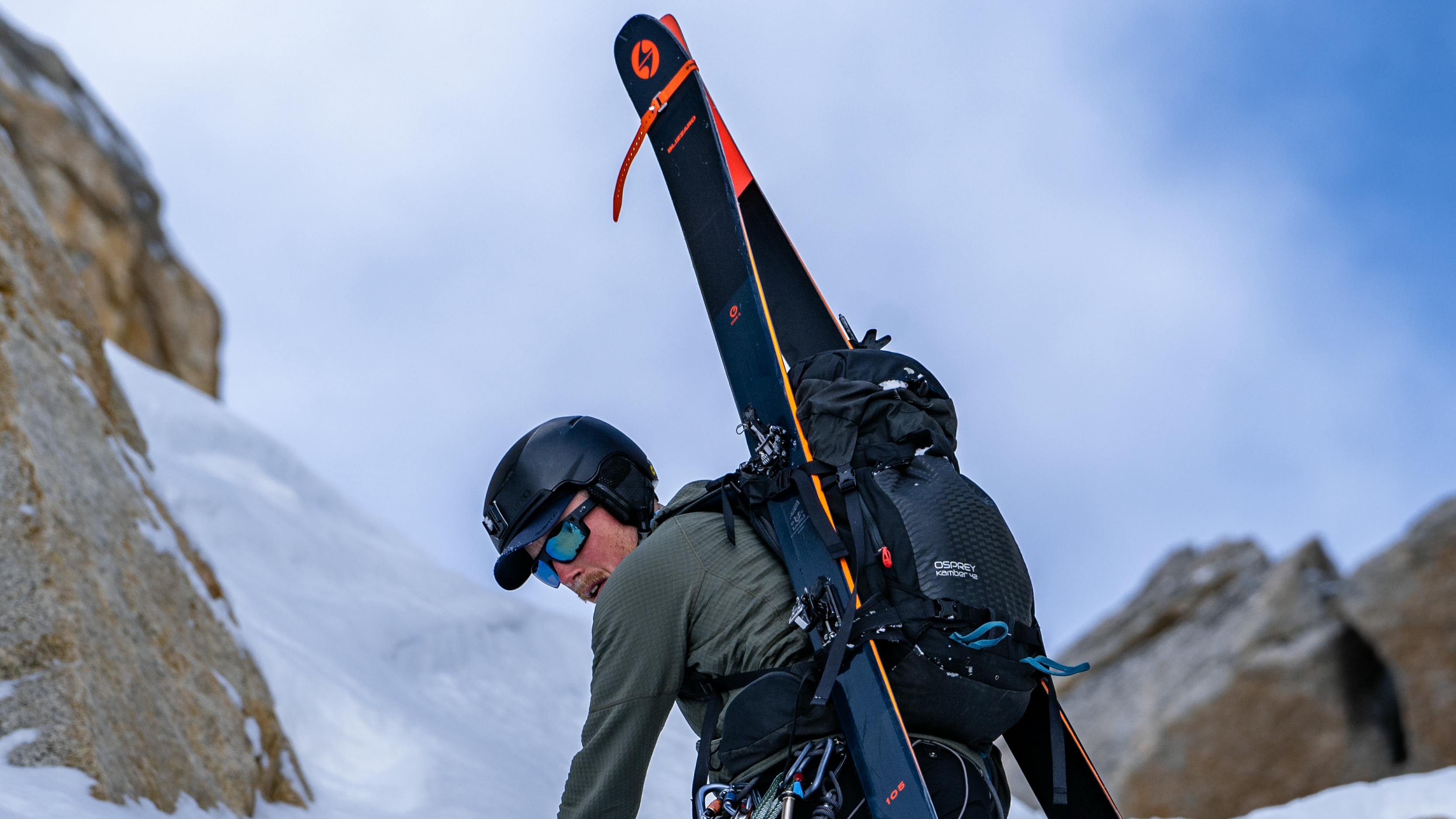 A skier hiking up a mountain with his Blizzard skis on his back.