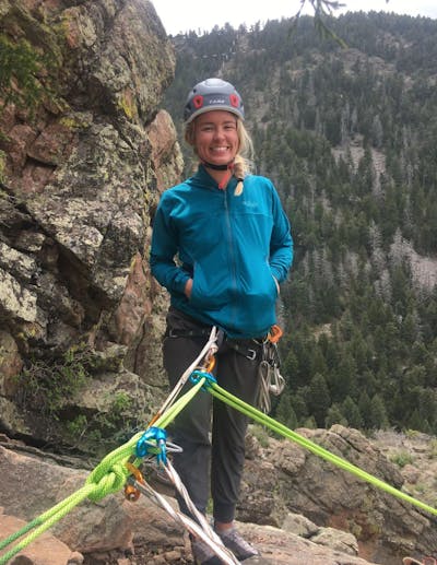 A woman smiling connected to some climbing gear. 