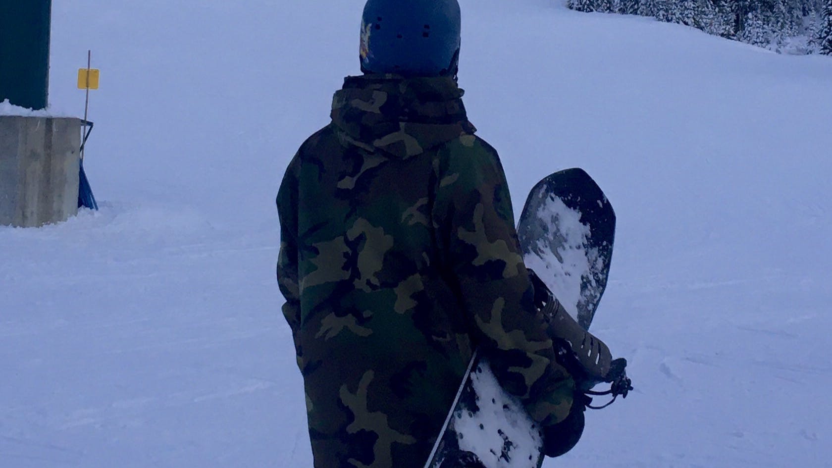 A man with a snowboard looks off at a snowy mountain in the distance.