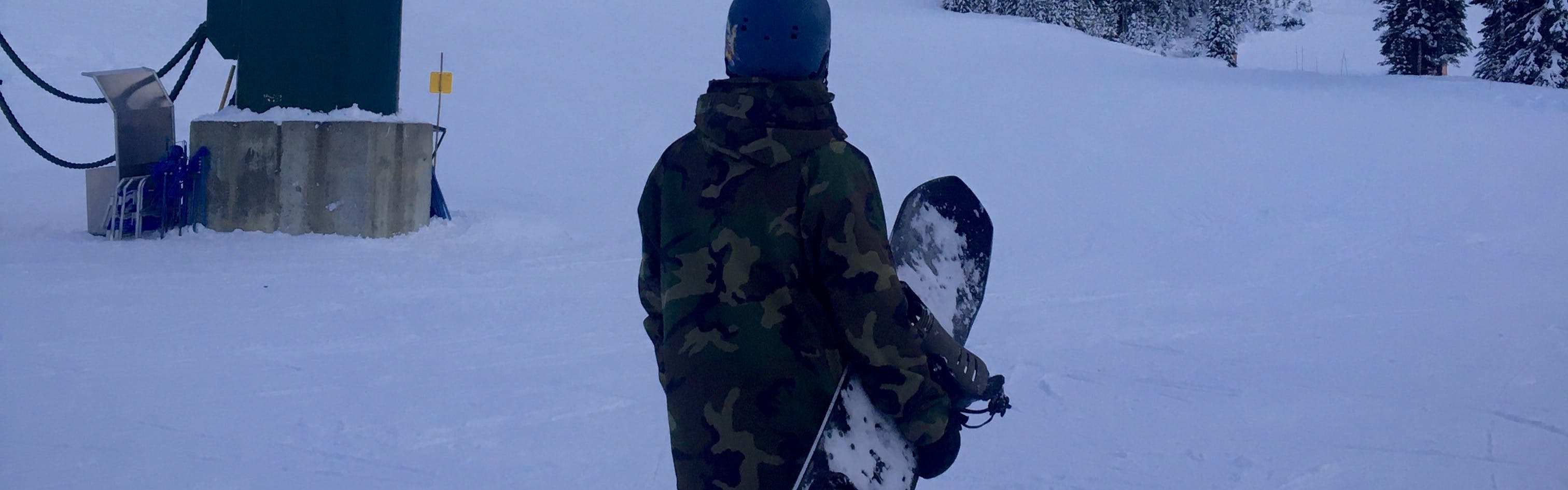 A man with a snowboard looks off at a snowy mountain in the distance.
