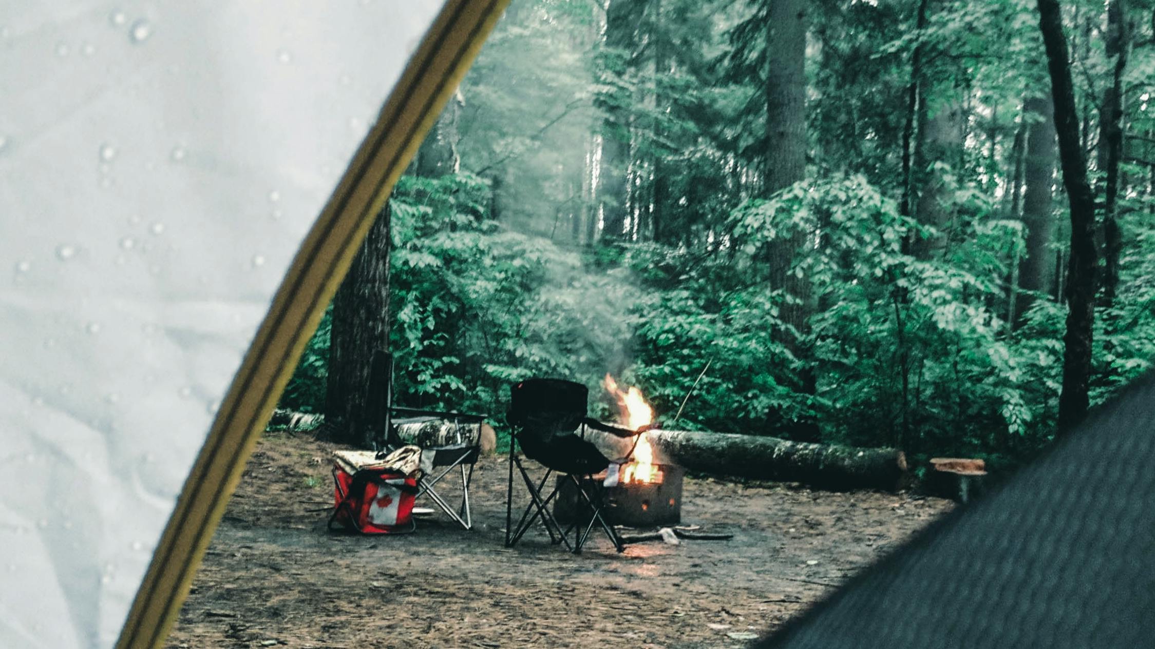 A rainy tent view of a chair and fire. 