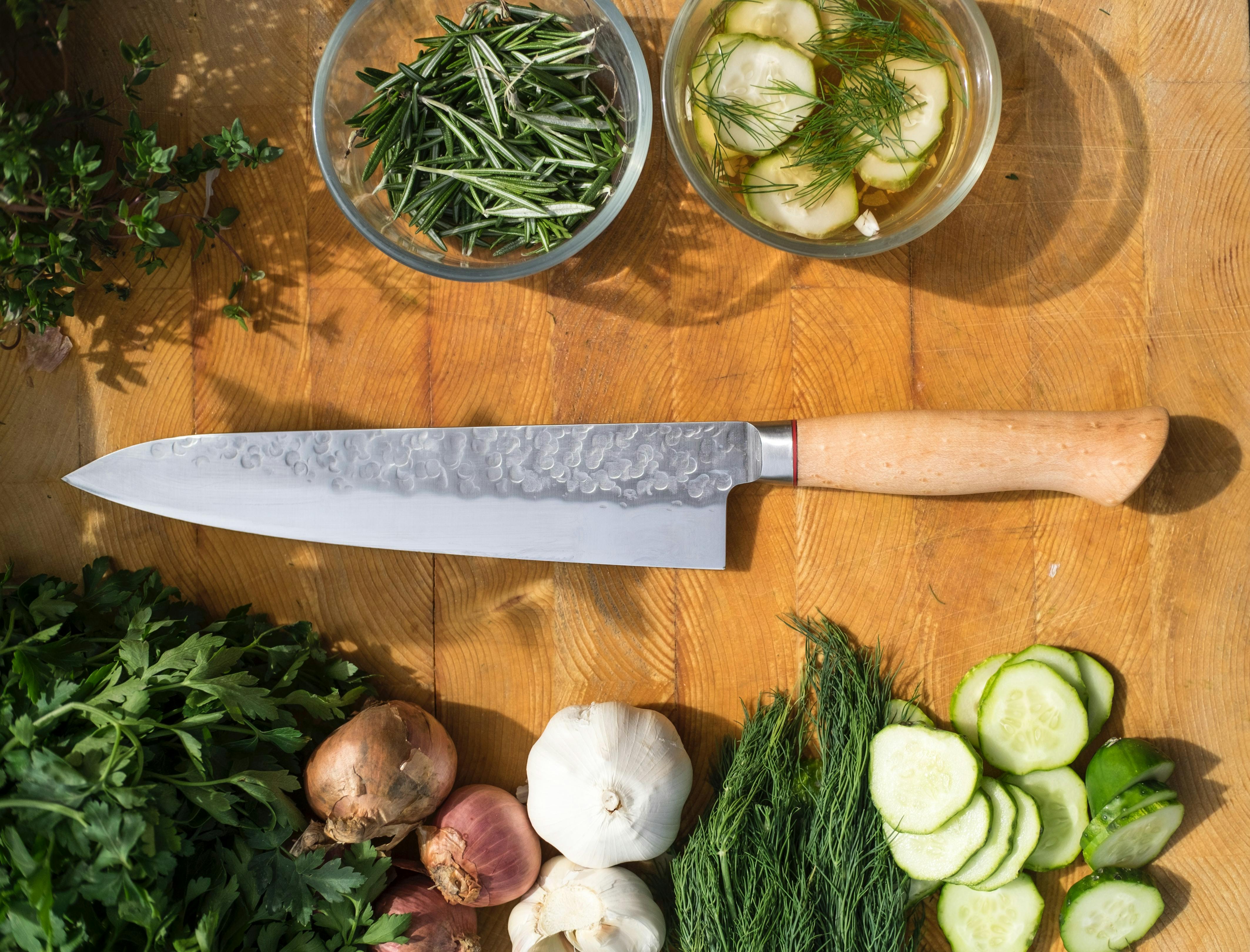 A knife lays next to some garlic and herbs.