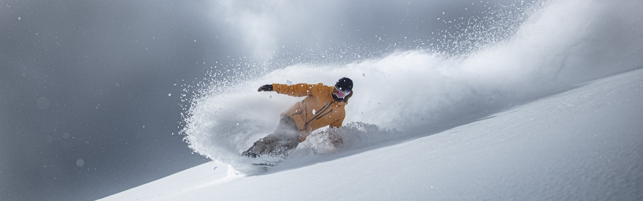A snowboarder in a yellow jacket sends up a huge spray of powder.