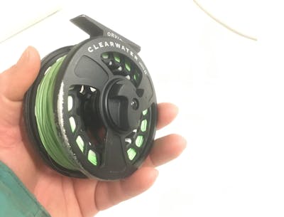 A hand holding the Orvis Clearwater LA Reel.