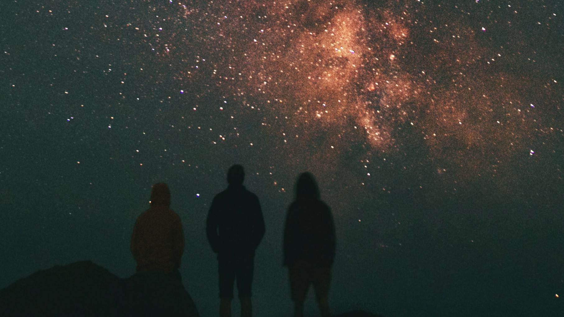 Three people stand looking at a starry sky. 