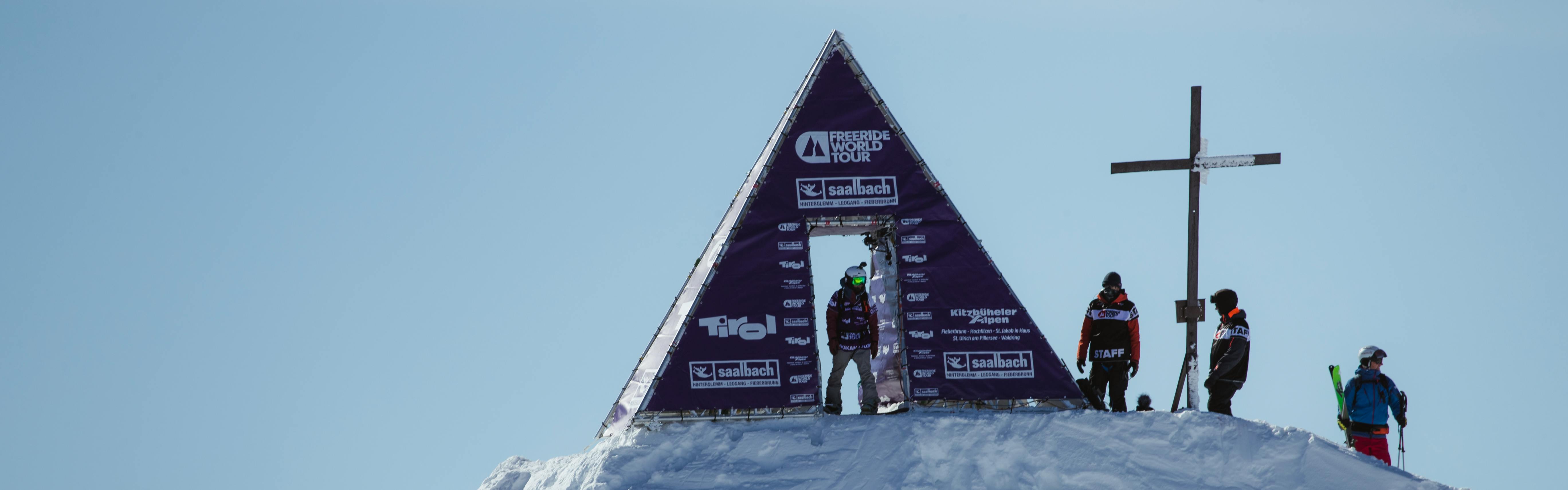 A snowboarder stands in the door of the purple A-frame FWT tent on top of the peak in Austria. 