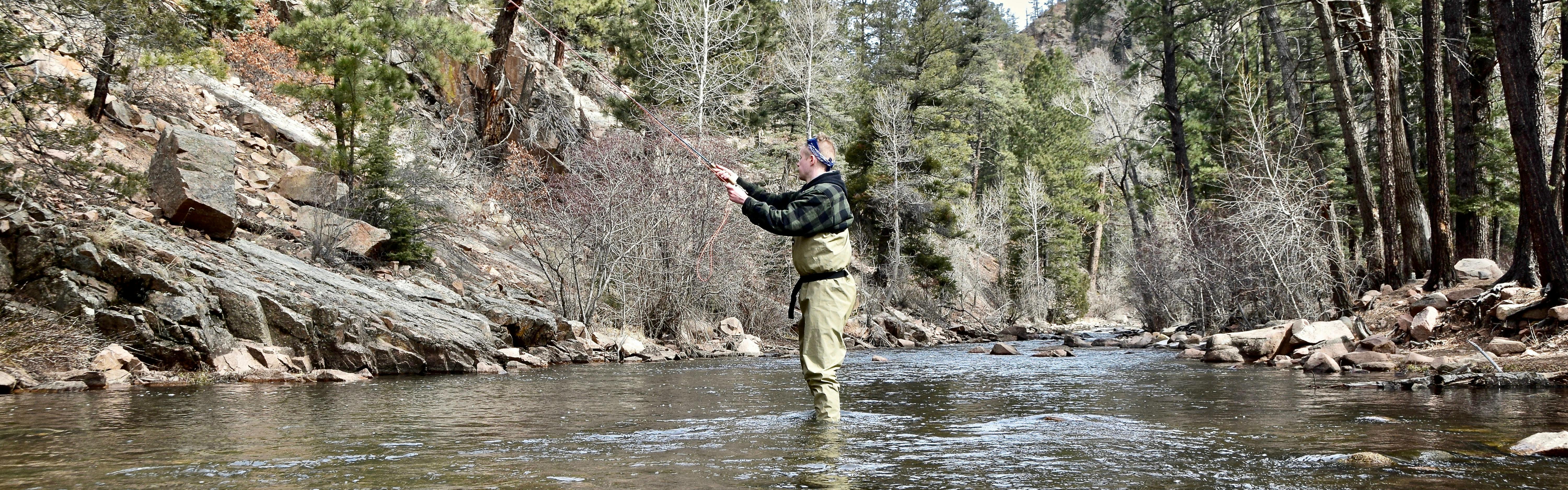 A man stands in a river in waders as he fly fishes.