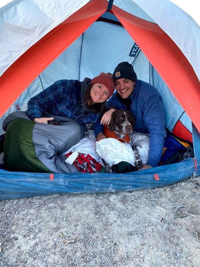 An image of the author, her husband, and their dog all smiling towards the entrance of their tent. They're snuggled up and cozy!