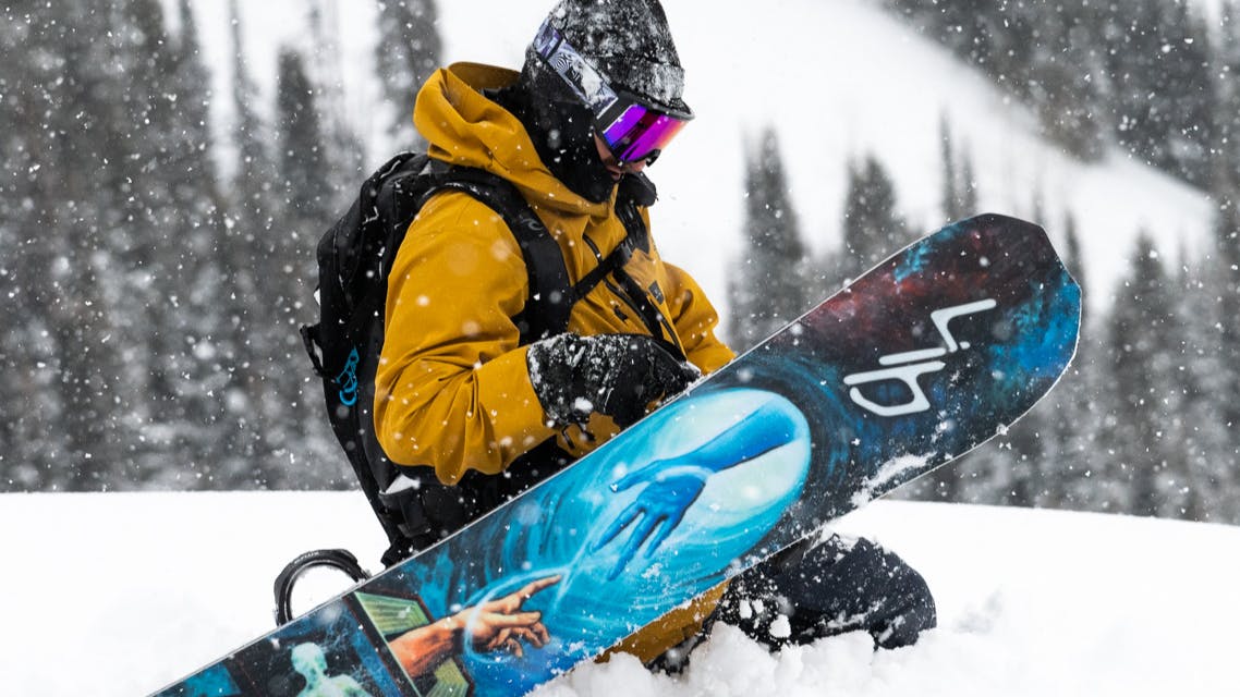 Someone kneels in the snow with their snowboard.