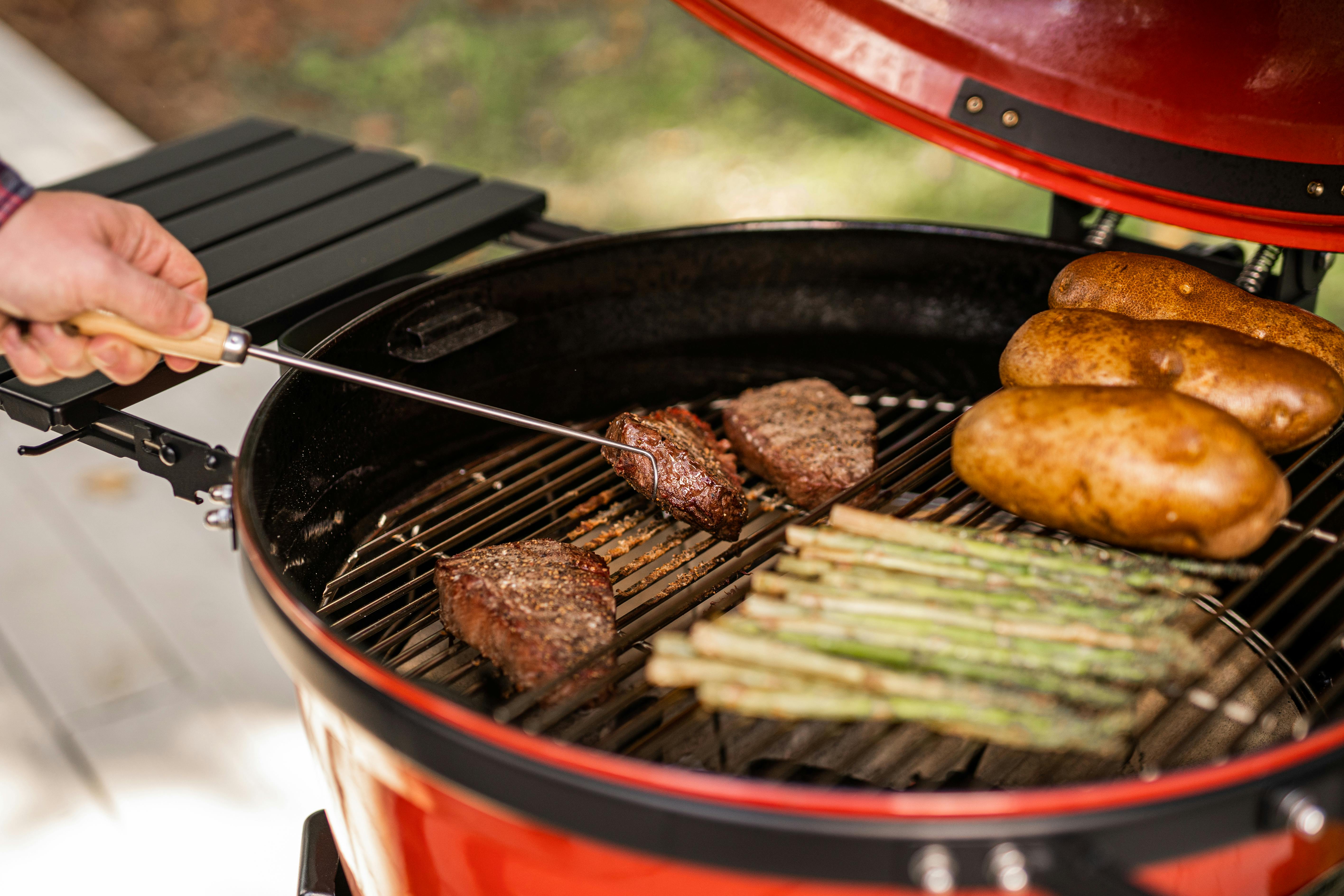 Someone cooking some potatoes, asparagus, and meat on a Kamado Joe Grill. 