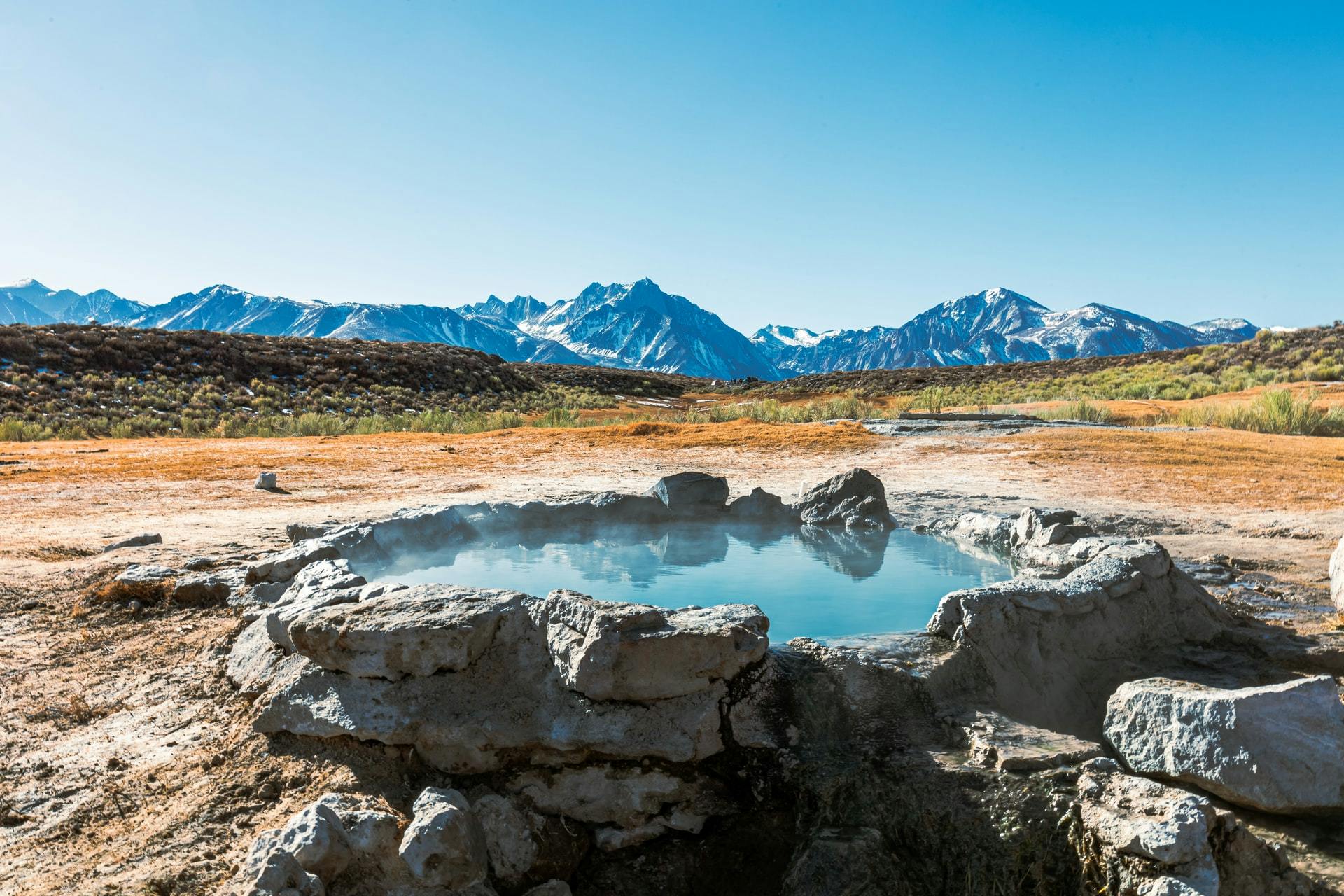 A hot springs with mountains and a field in the background.