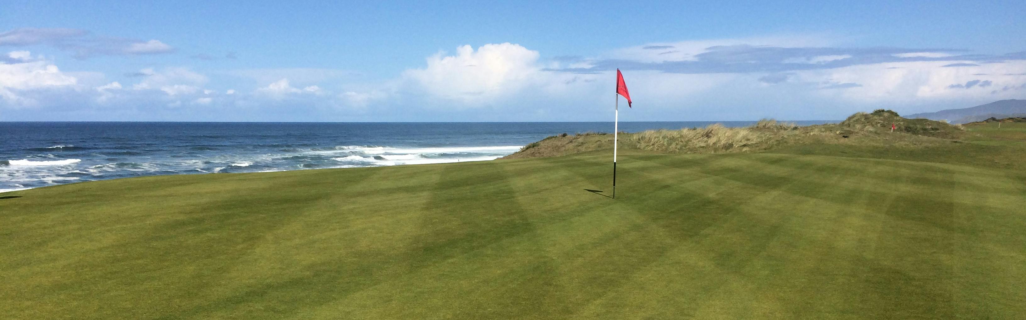 A flag on a golf course with the ocean in the background