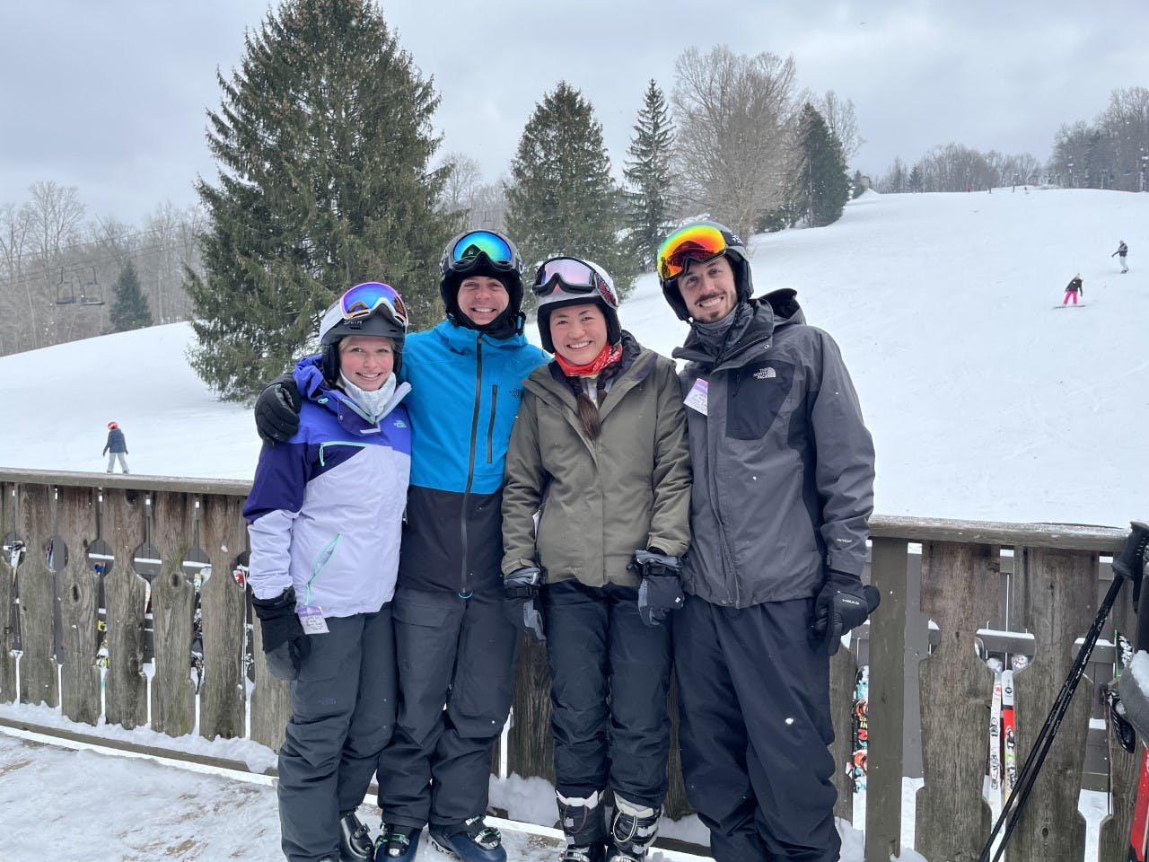 Four people in ski gear stand smiling at the bottom of a ski run. 