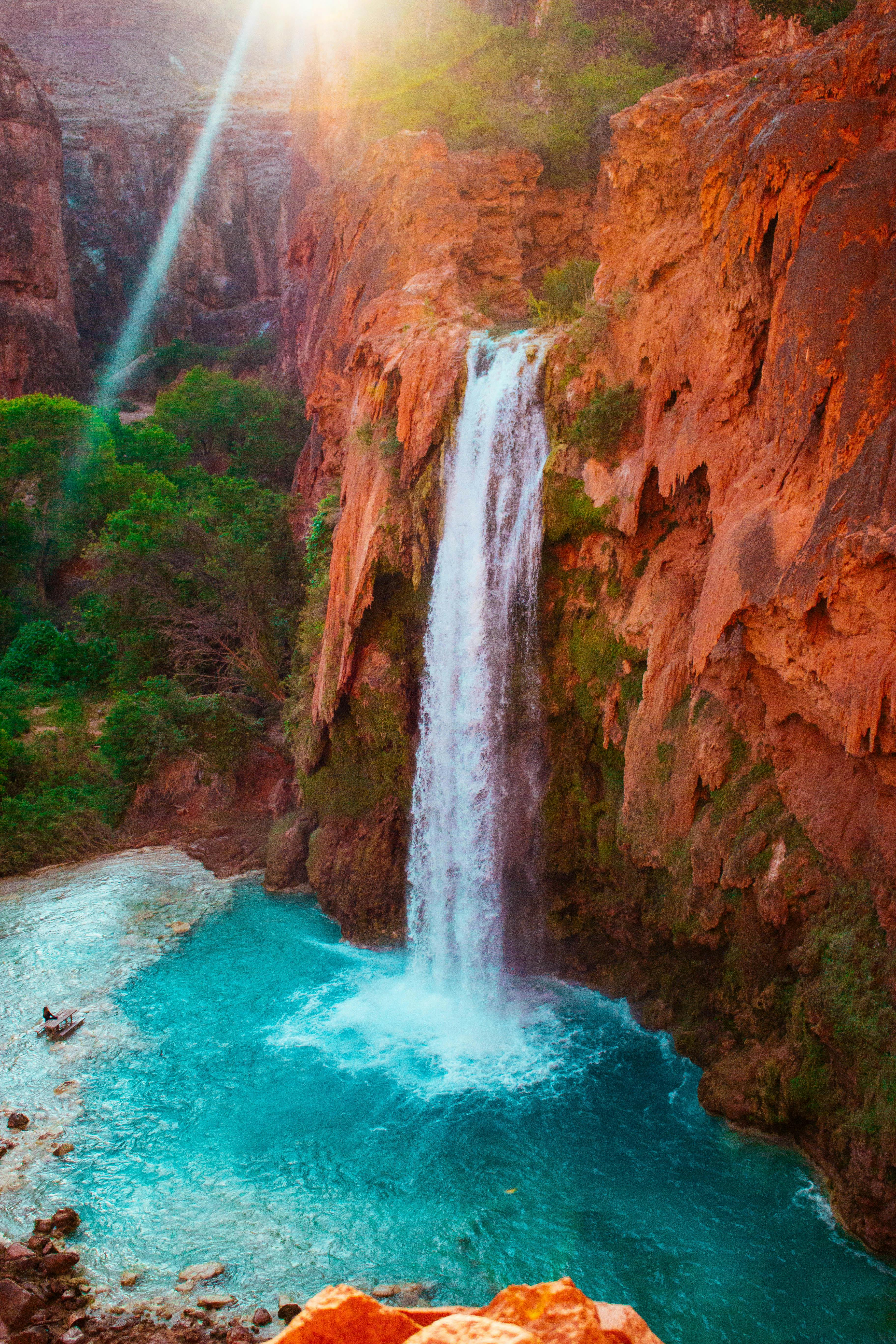 A waterfall descends over red rocks into a blue pool
