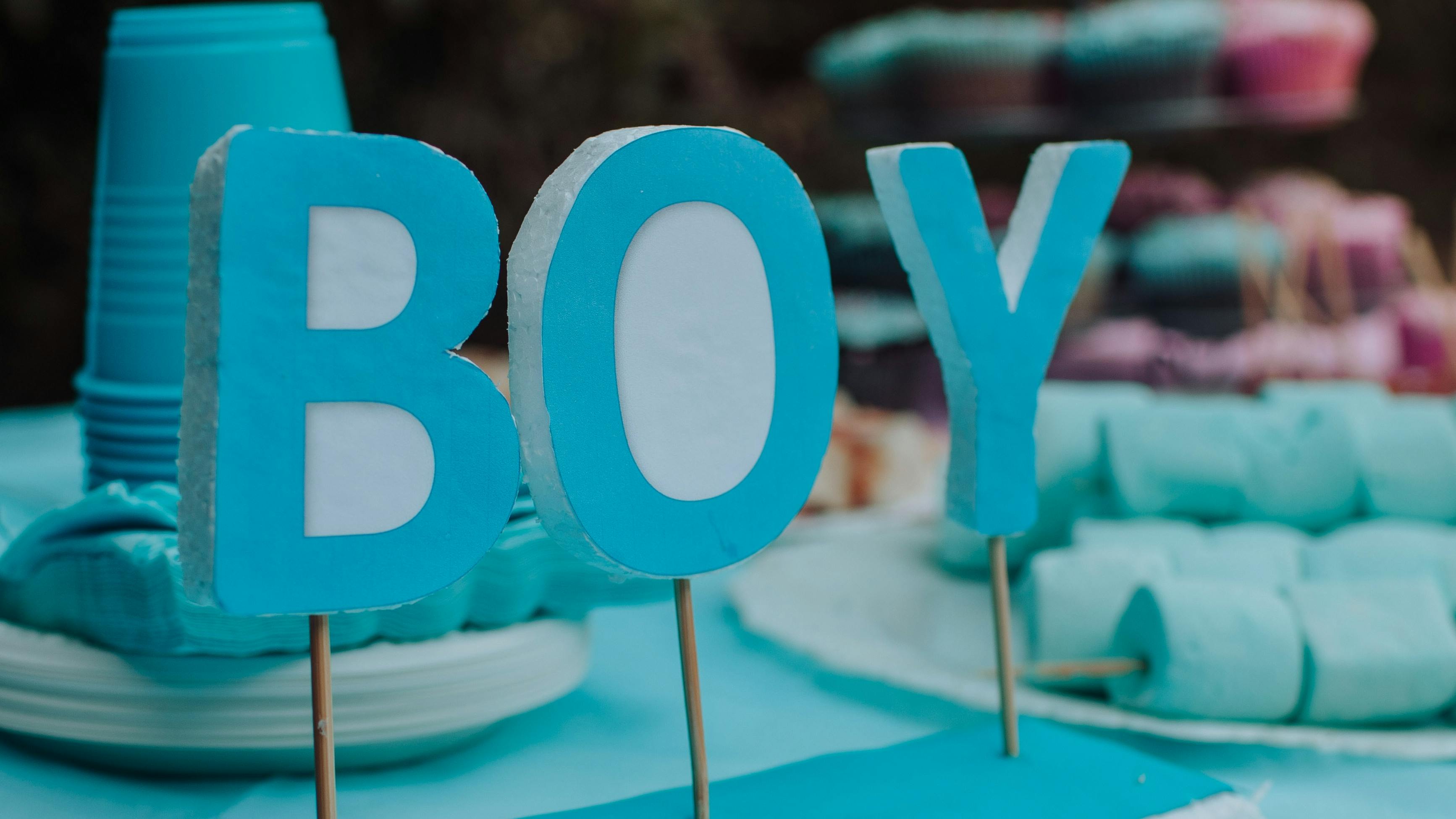 A party table that has blue cupcakes and cups and a sign that says "BOY".