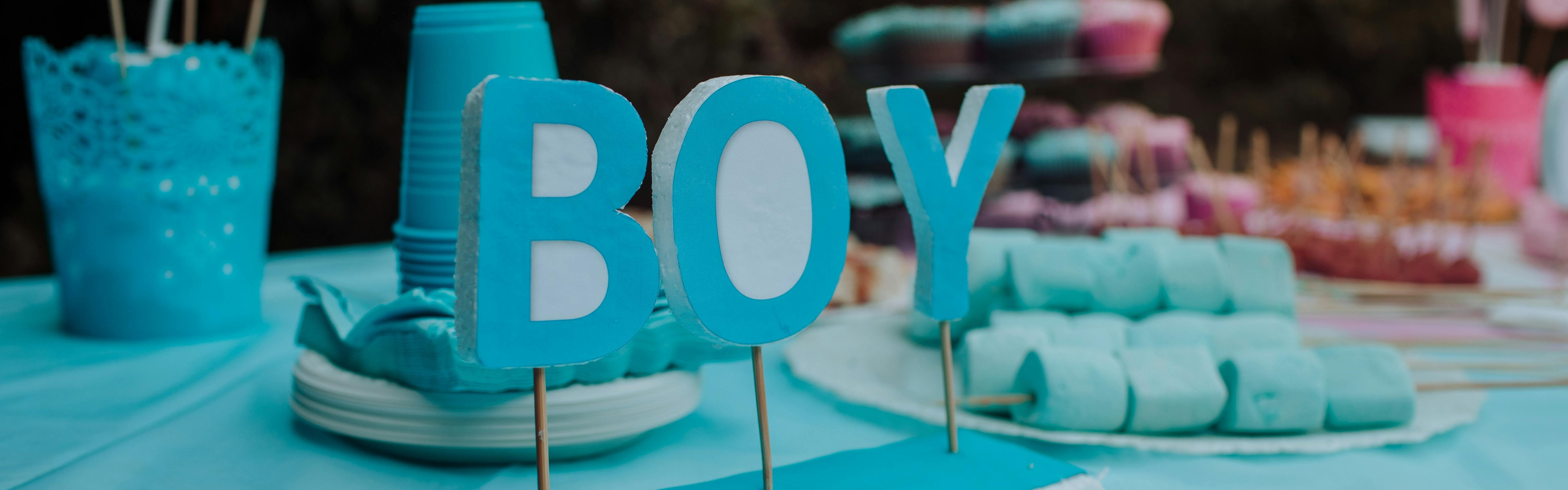 A party table that has blue cupcakes and cups and a sign that says "BOY".