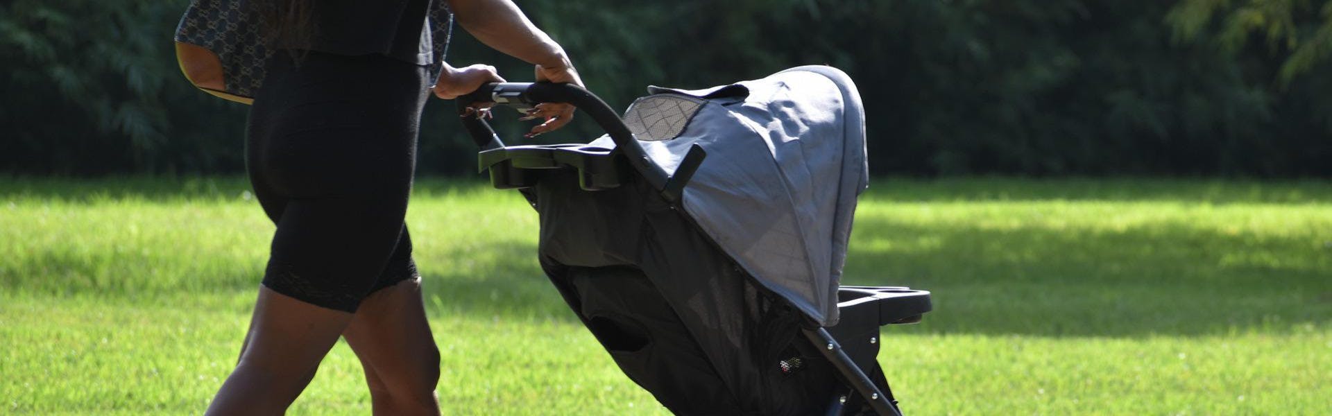 A woman with a bag pushes a baby stroller.