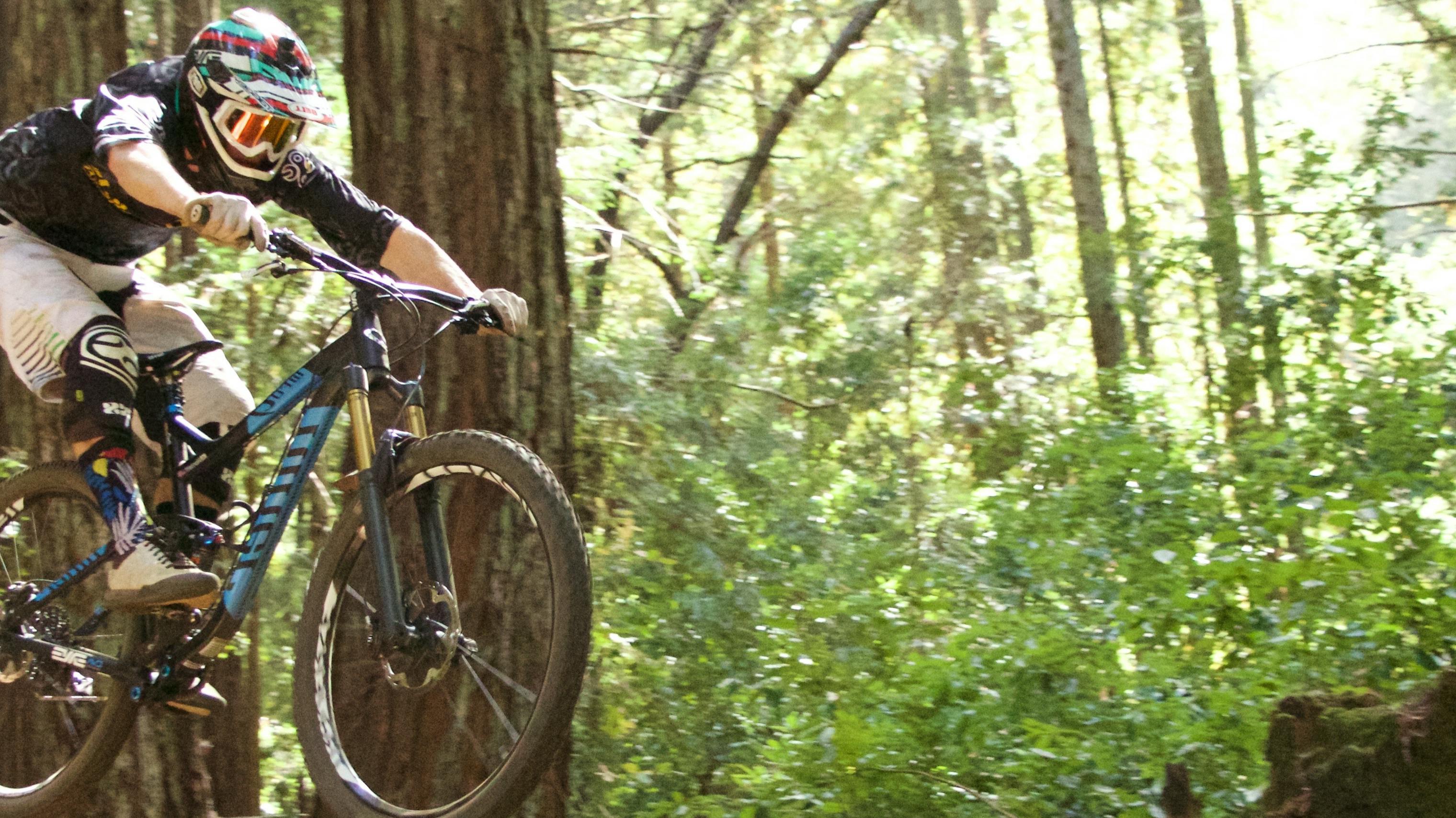 Curated expert Mitch Harnett airborne with his mountain bike in the forest in Santa Cruz, CA