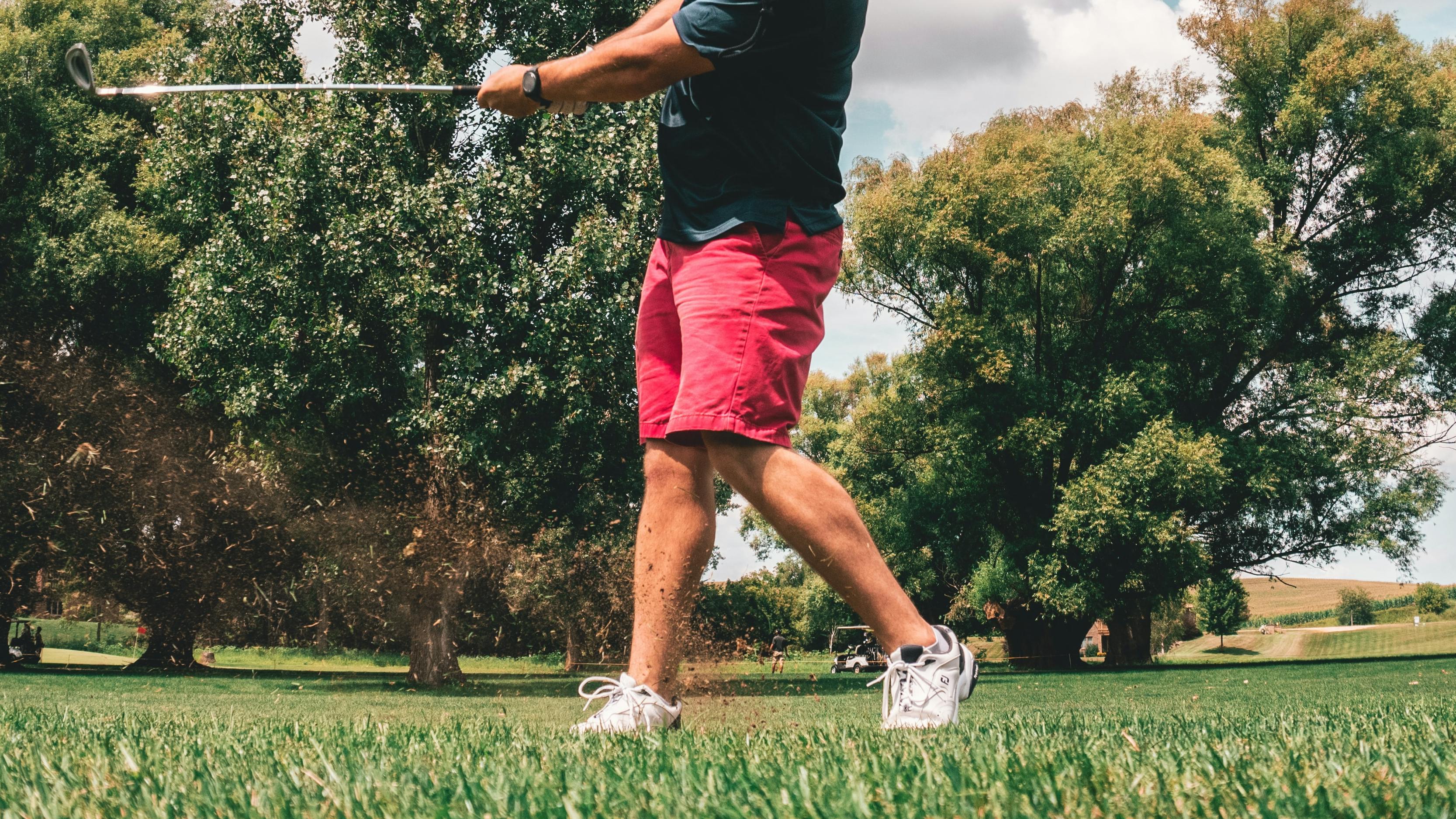 A man takes a swing at a golf ball with an iron. 