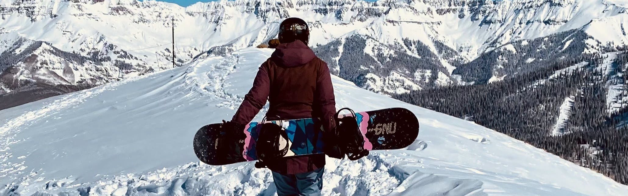 A snowboarder hiking with the GNU Velvet Snowboard. 