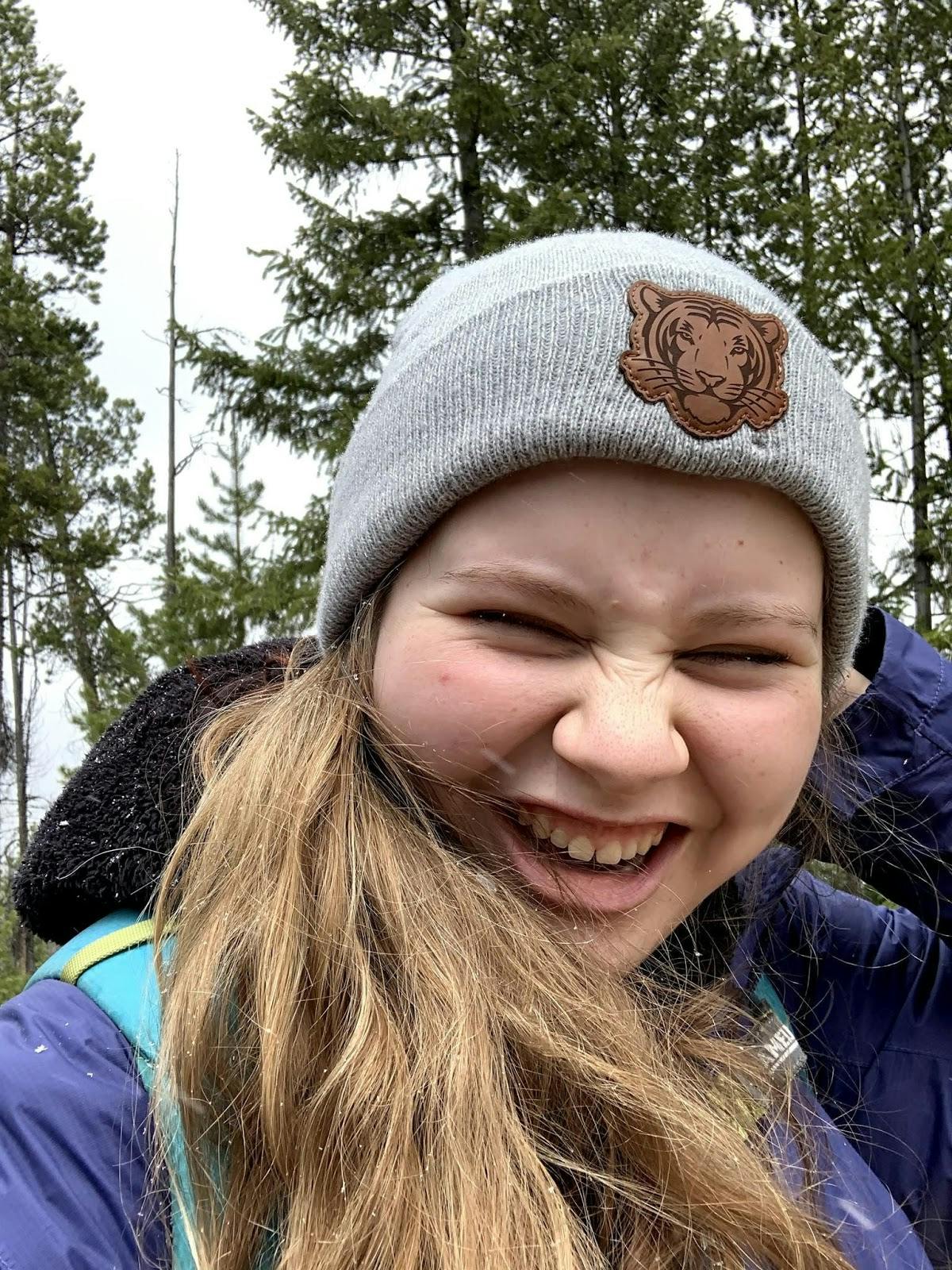 The author takes a selfie, smiling and scrunching up her face while wearing a beanie, rain coat, fleece, and a backpack. 