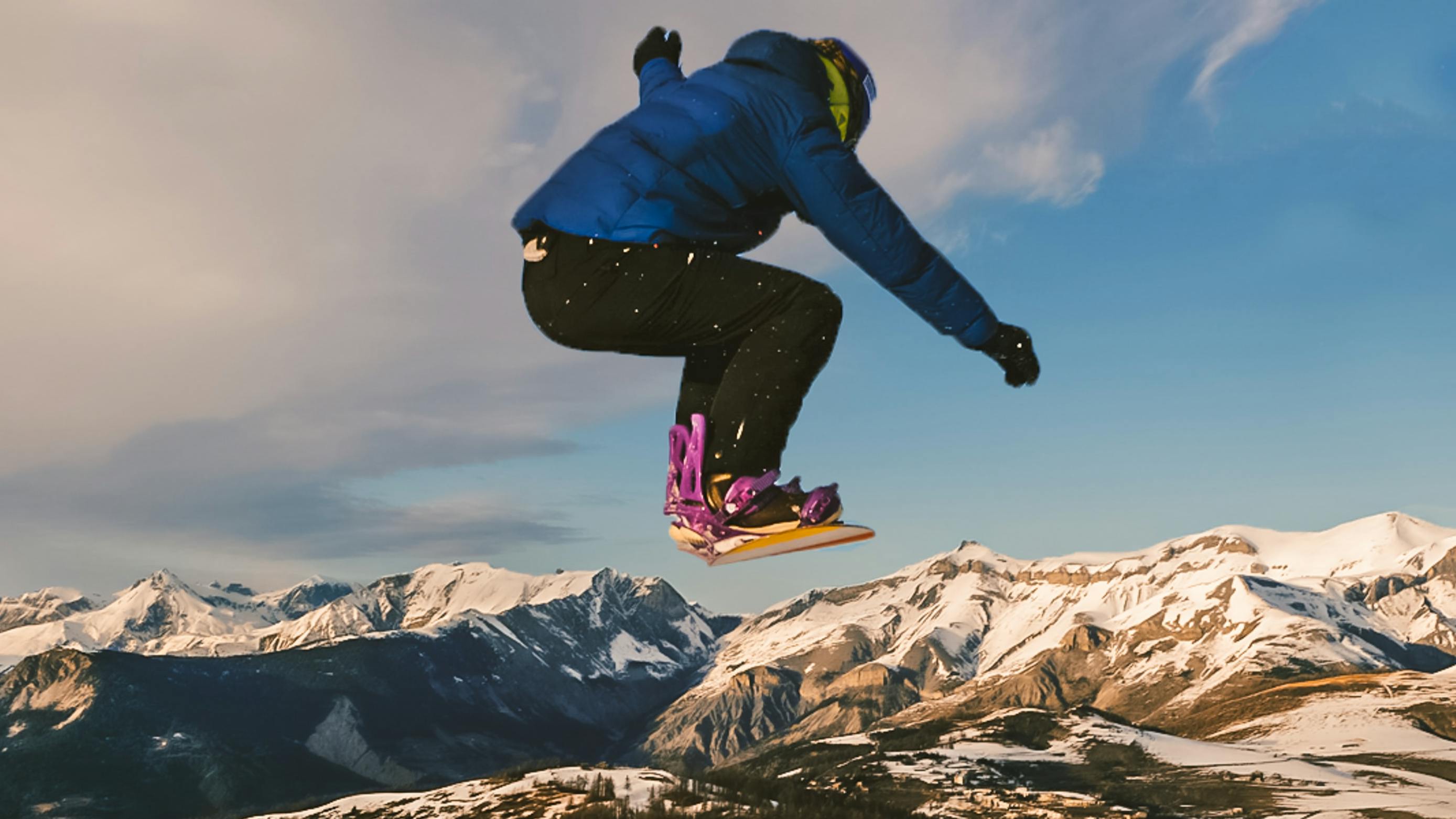 A snowboarder jumps and a mountain range opens up in front of him. 