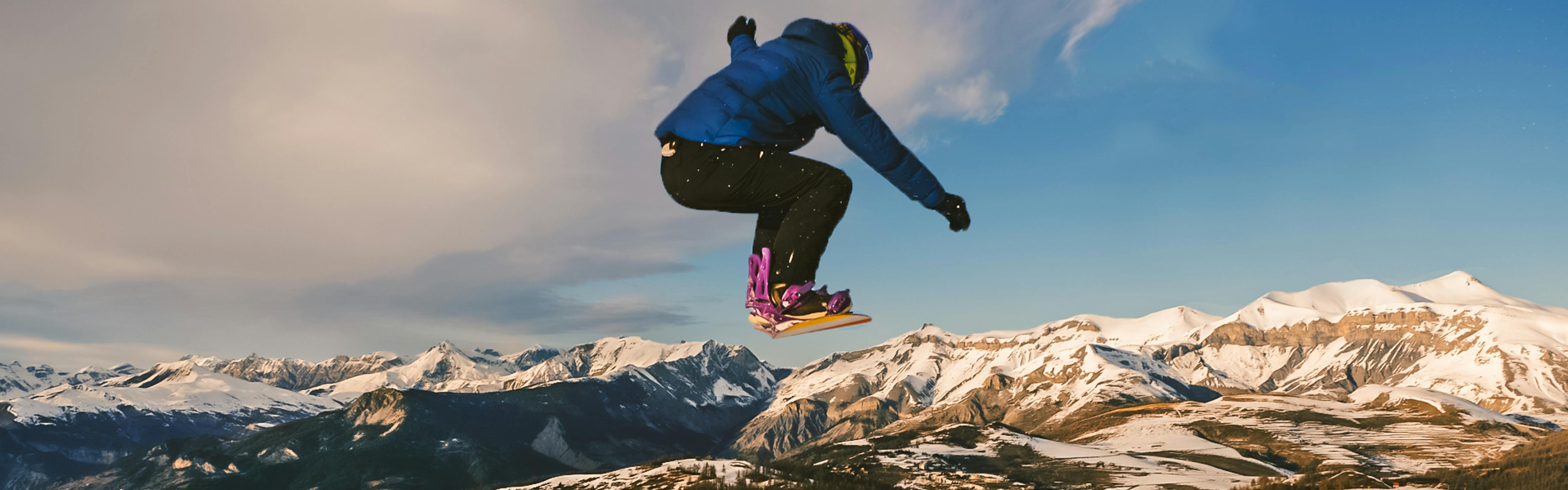 A snowboarder jumps and a mountain range opens up in front of him. 