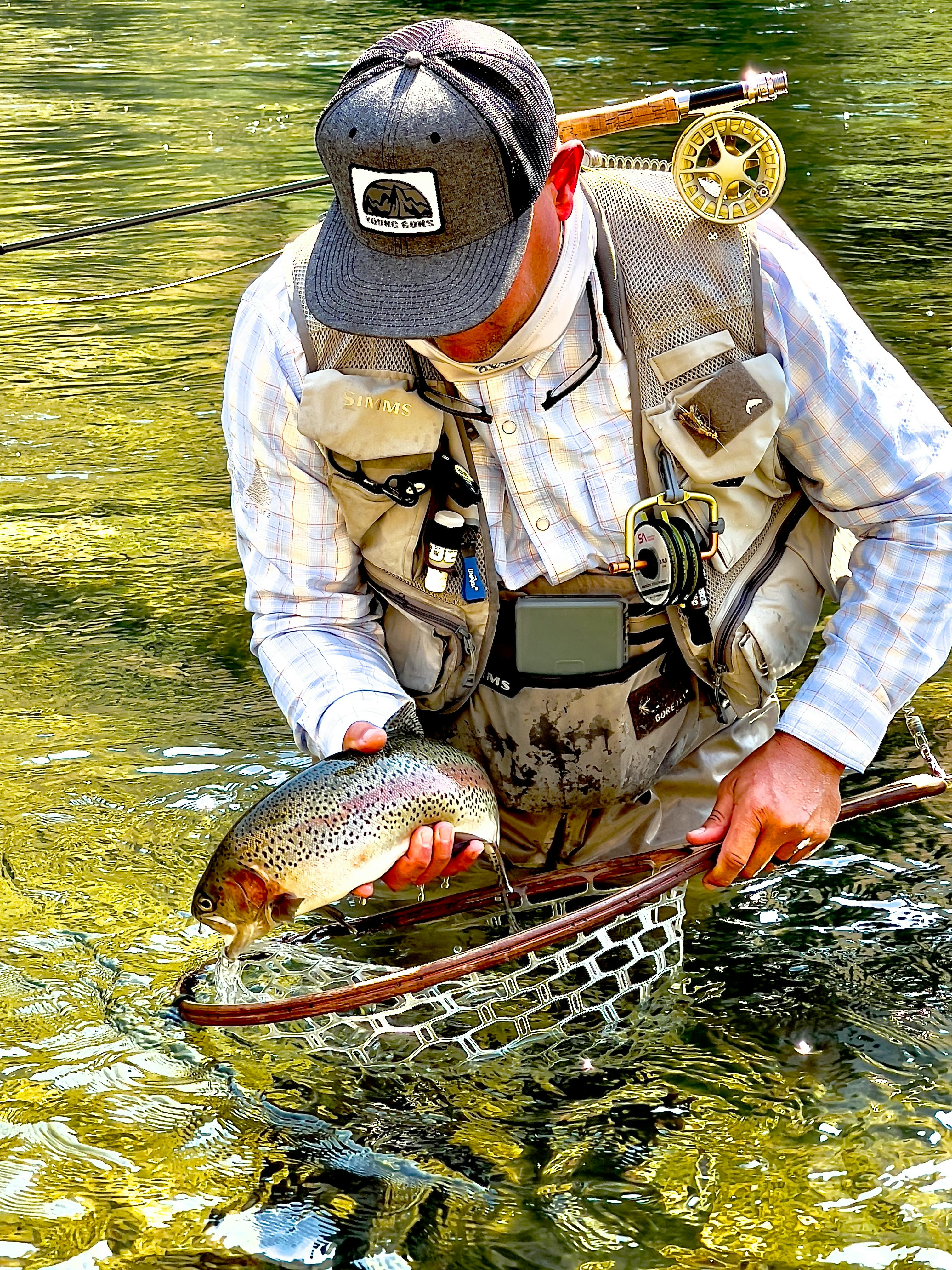 A man holding a large fish in his fishing net while wearing the Orvis Pro Stretch shirt. 