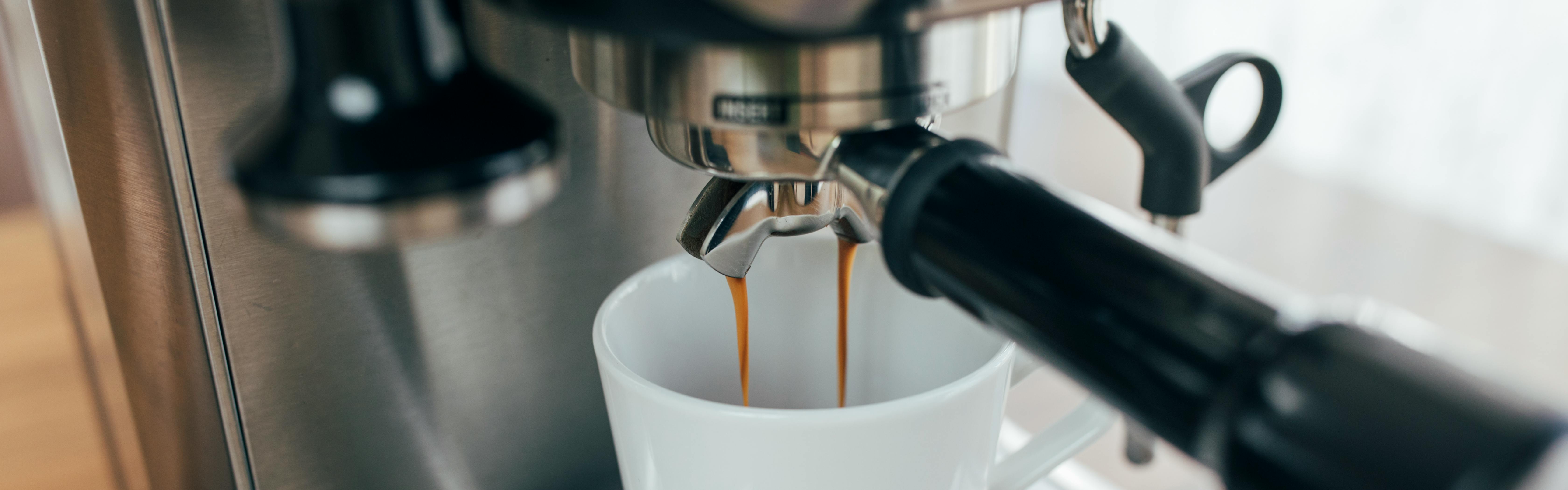 A shot pours from a prosumer espresso machine into a white ceramic mug.
