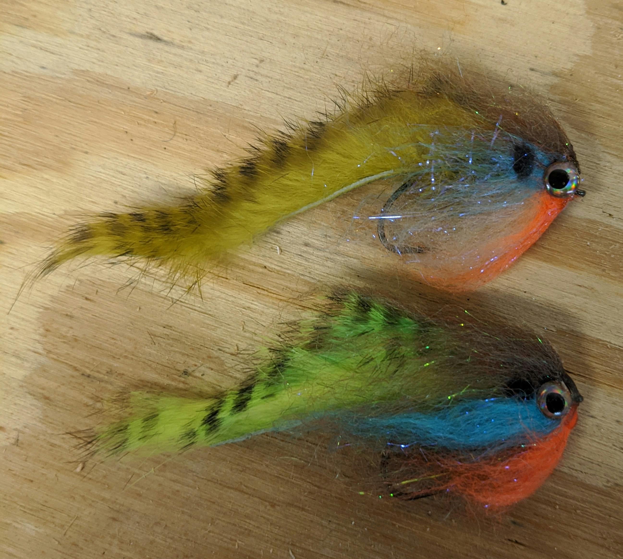 Two bluegill imitation streamers lying on a wood counter.